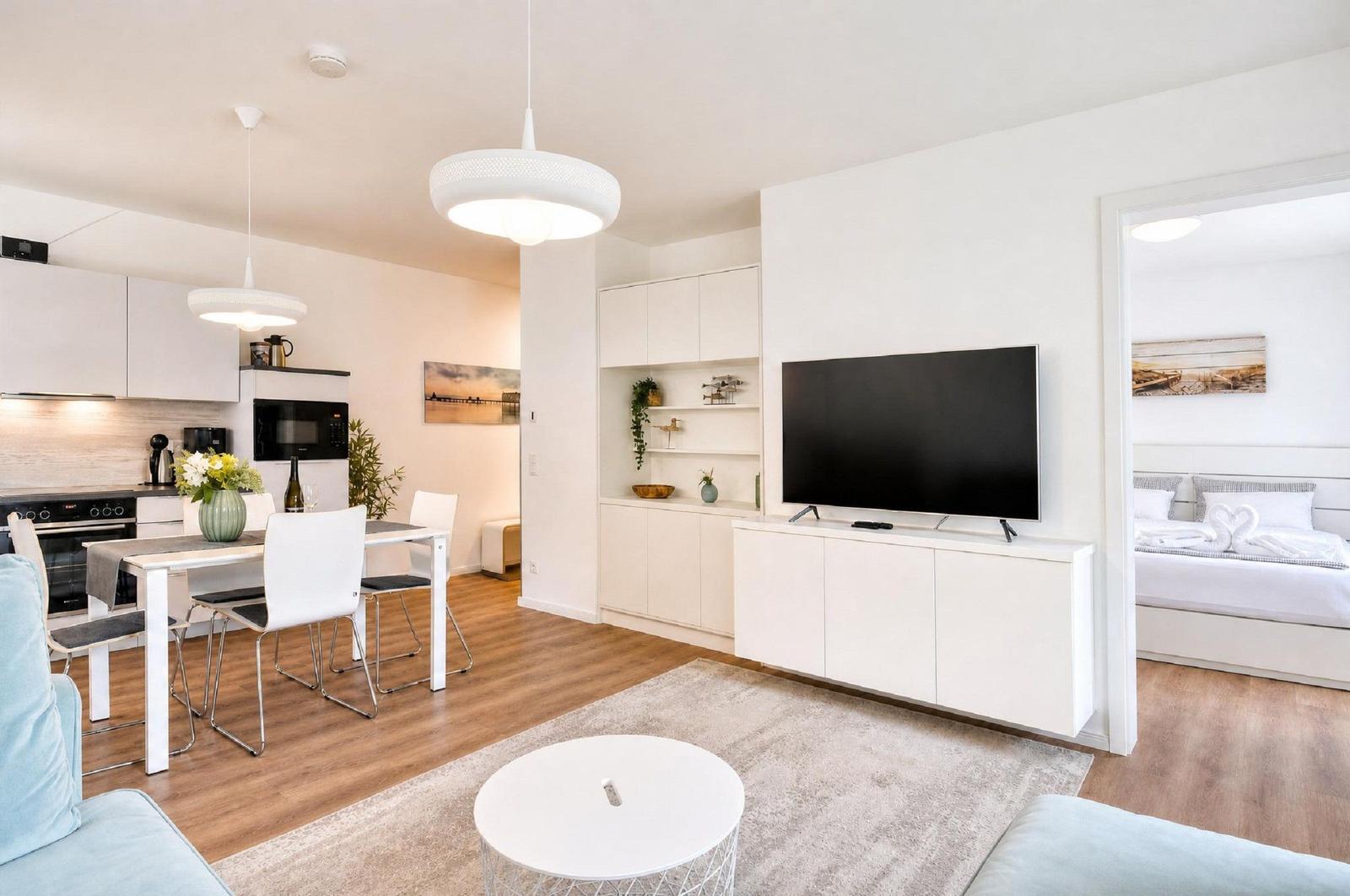 Wohnung mit Küche, Essbereich, TV und Schlafzimmer. Moderne Einrichtung mit Holzboden und weißen Möbeln.