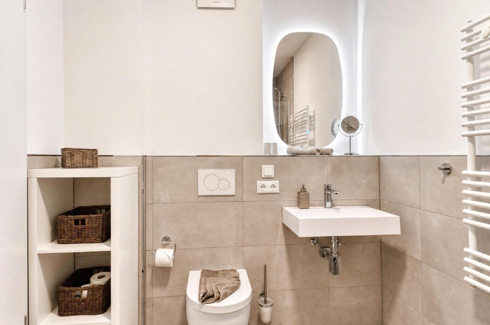 Badezimmer mit Toilette, Waschbecken und Spiegel. Regal mit Körben und Heizkörper.