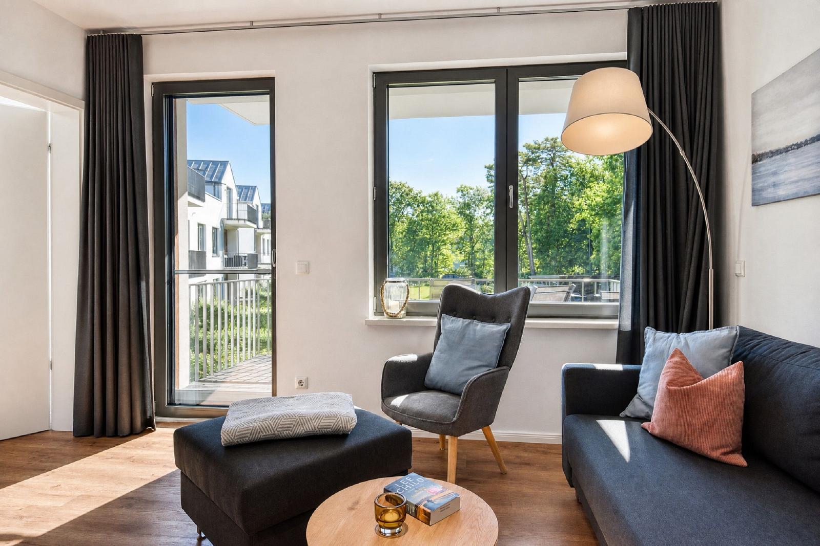 Wohnzimmer mit Sofa, Sessel und Blick auf Balkon und Grünanlagen.