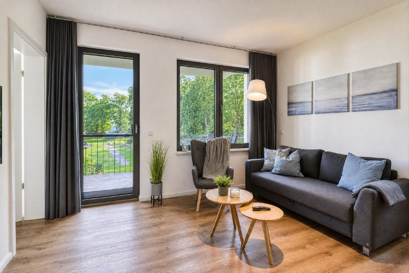 Wohnzimmer mit Sofa, Sitzgelegenheit und Blick auf Balkon und Grünfläche.