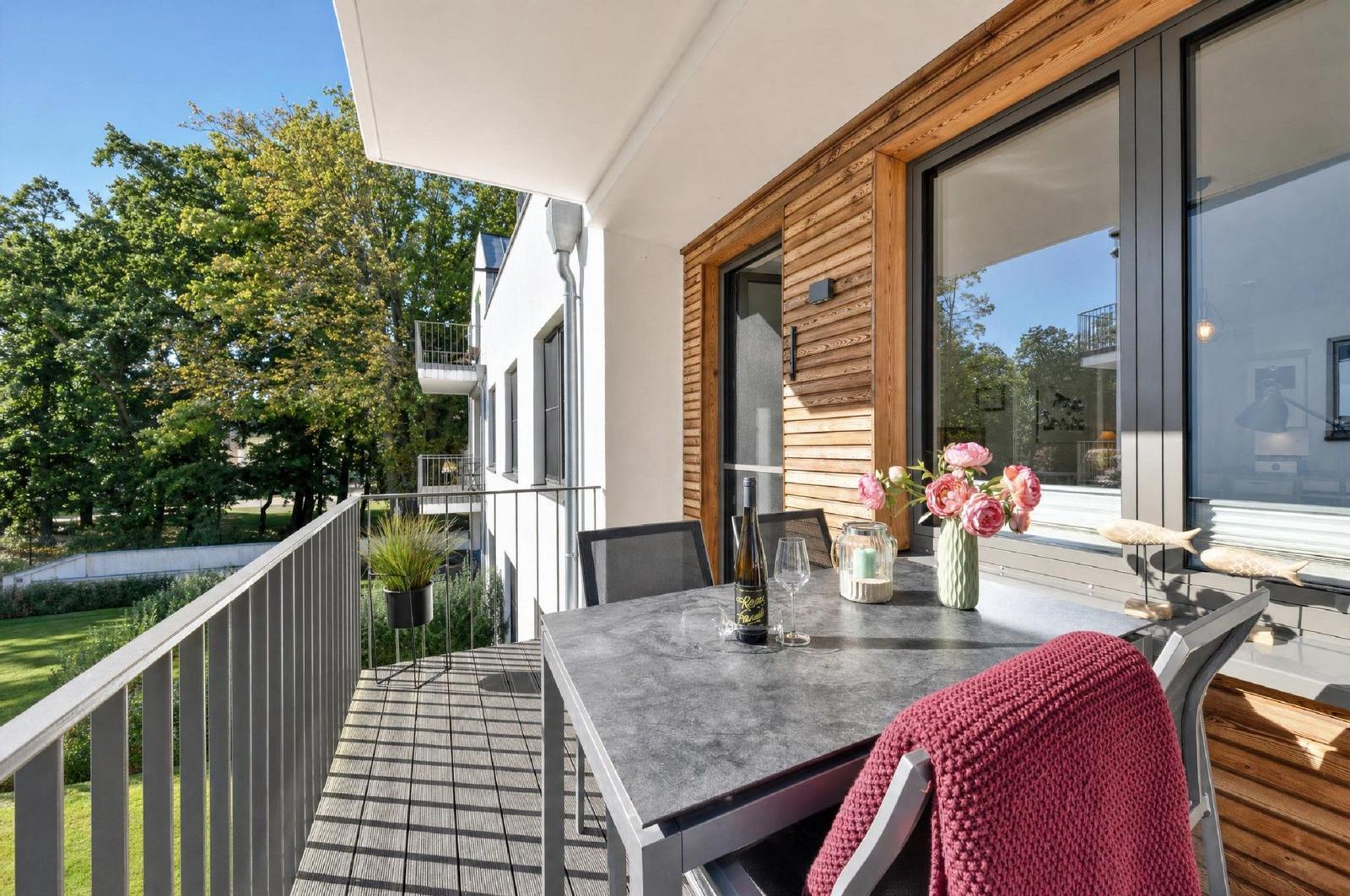 Terrasse mit Tisch, Stühlen und Blumen. Blick auf grüne Bäume und benachbarte Häuser.