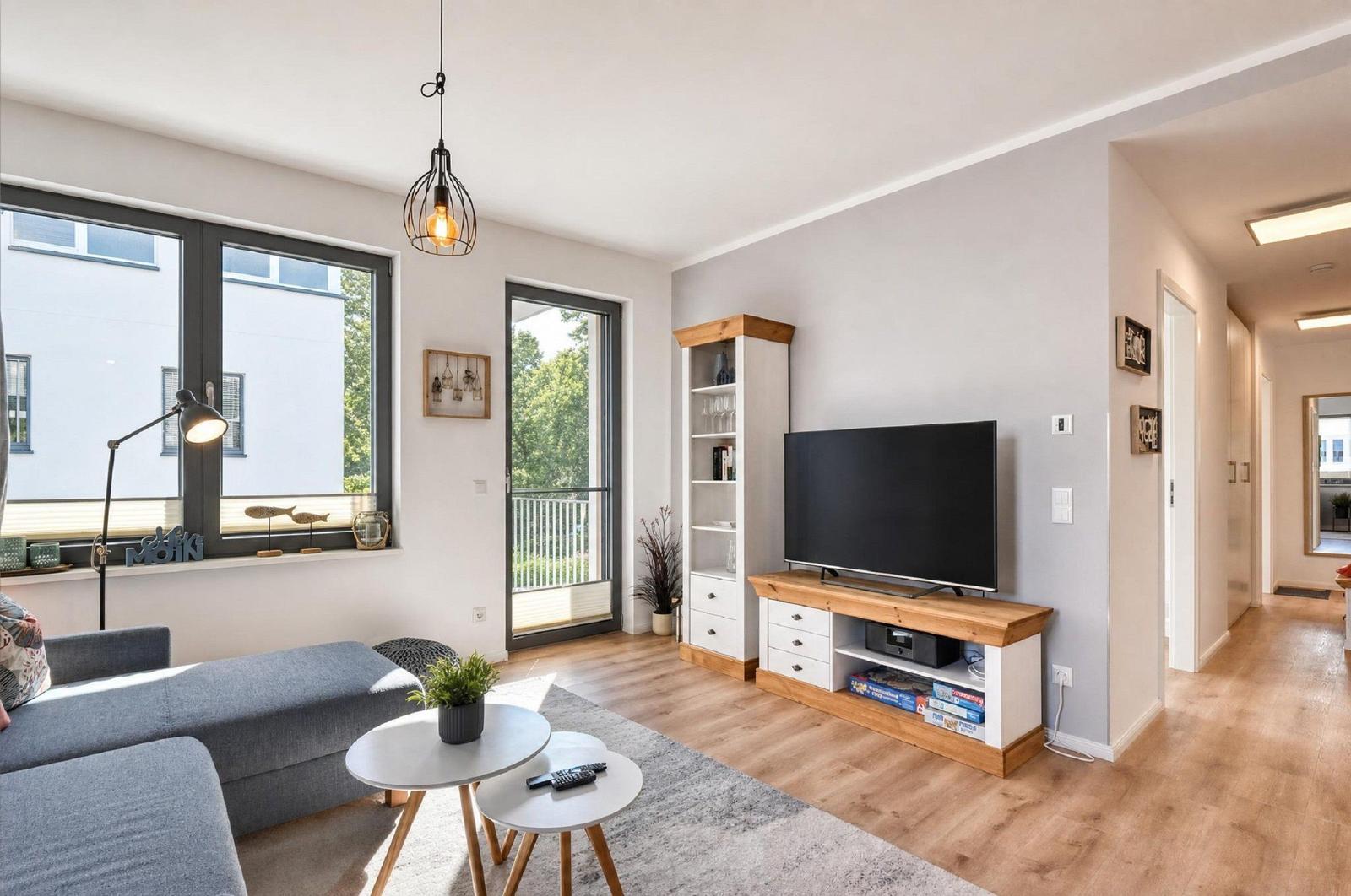 Wohnzimmer mit Sofa, Fernseher und Balkontür. Holzmöbel und große Fenster.
