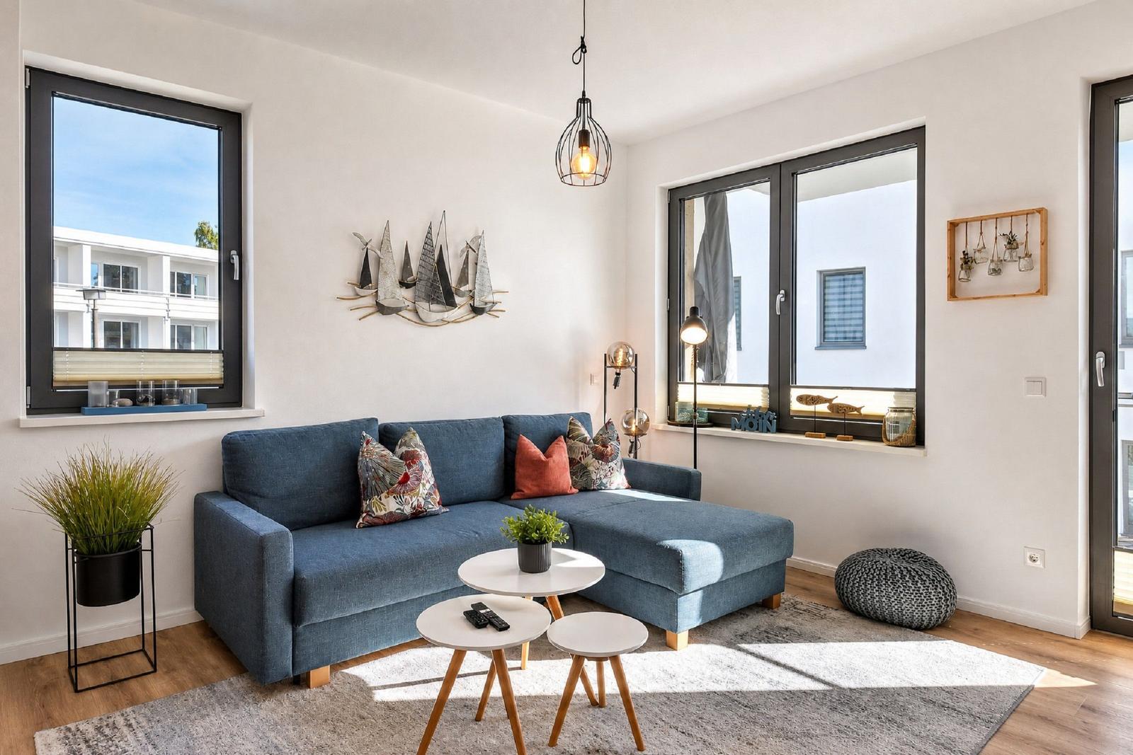 Ein Wohnzimmer mit blauem Sofa, drei runden Tischen und großen Fenstern.
