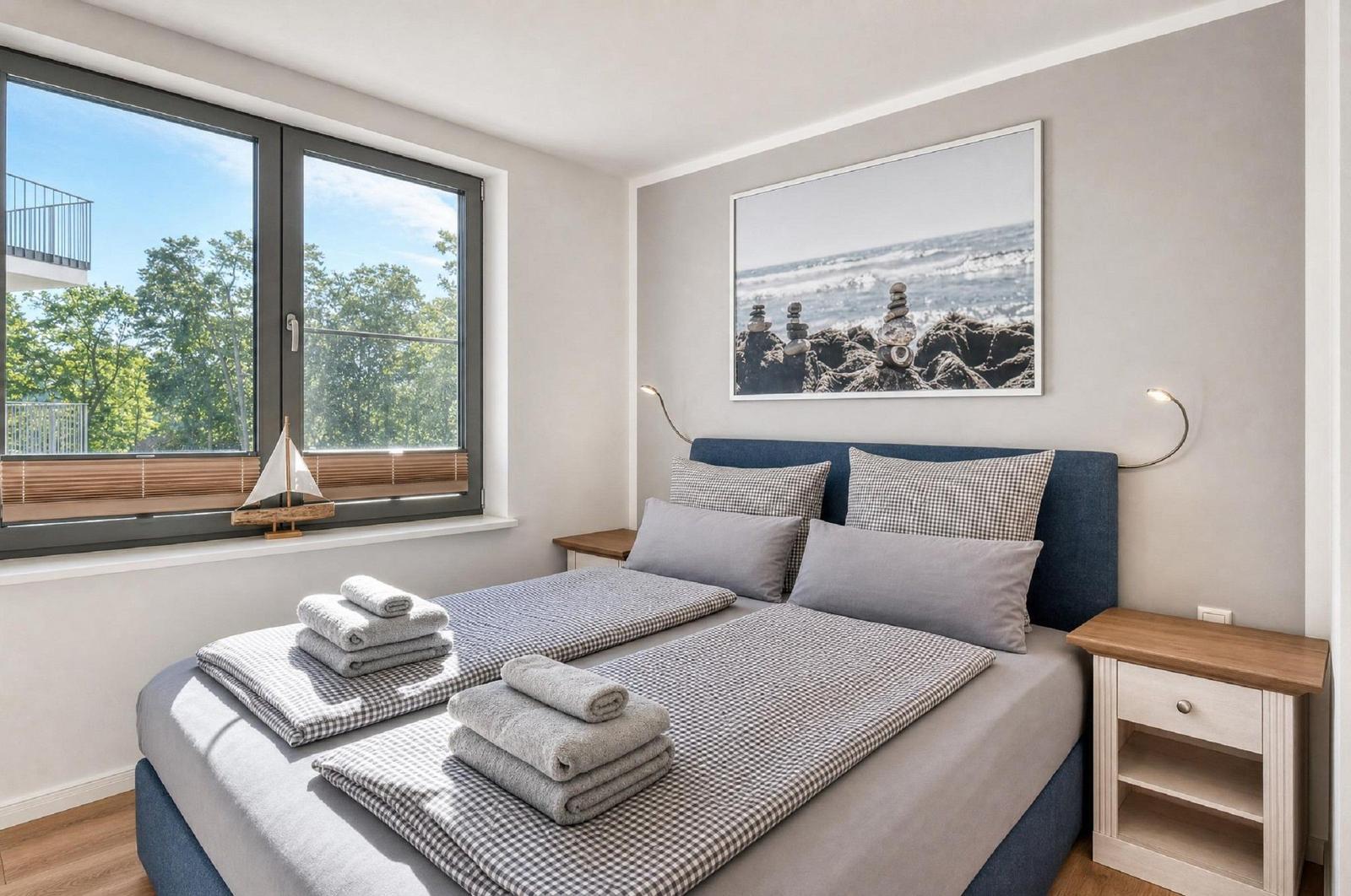 Schlafzimmer mit Doppelbett, Fensterblick auf Bäume und Wandbild mit Strandmotiv.