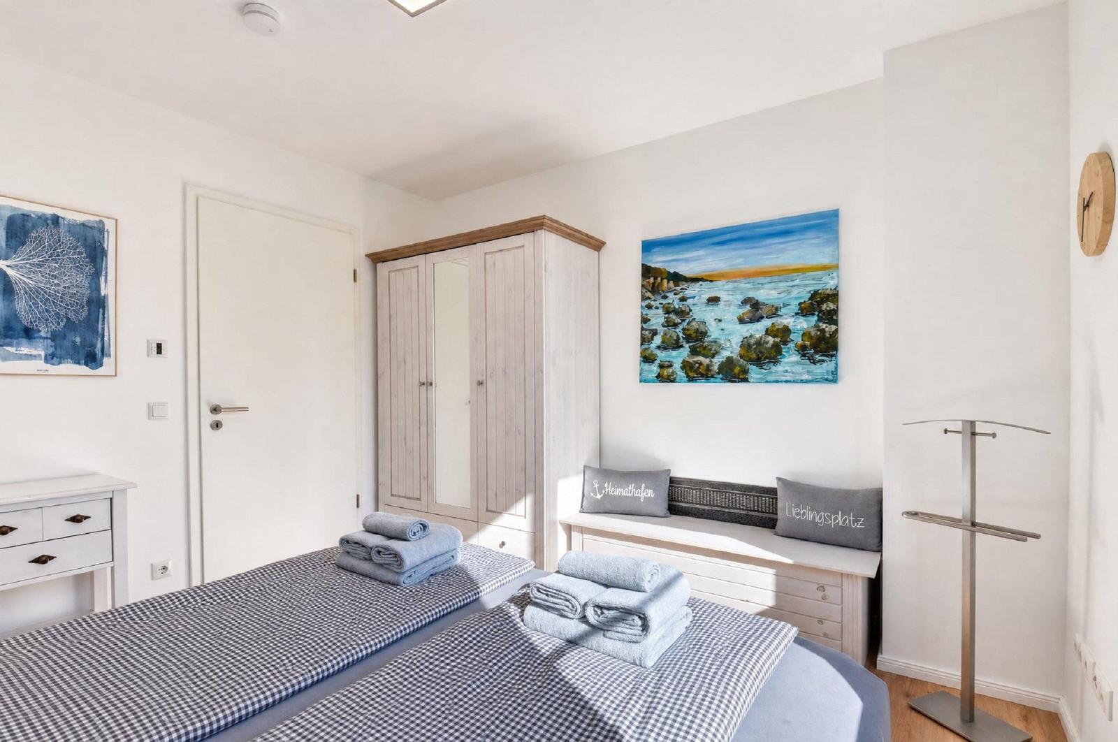 Zimmer mit Doppelbett, Kleiderschrank, Wandbild und Stehkleiderständer.