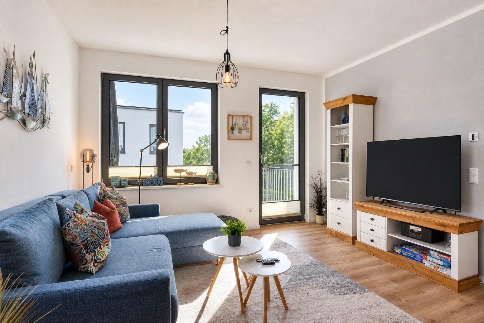 Ein Wohnzimmer mit blauem Sofa, Fernseher und großen Fenstern.
