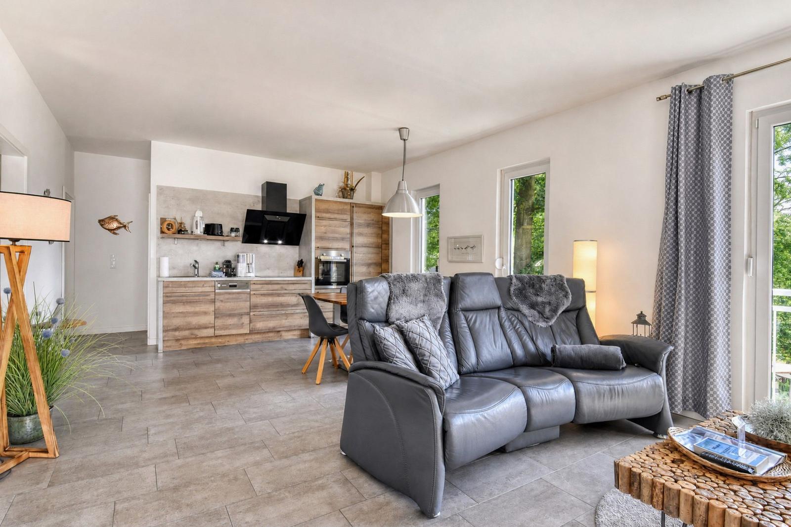 Wohn- und Küchenbereich mit grauem Ledersofa und Holzmöbeln.