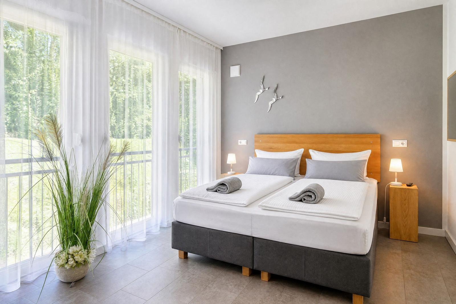 Schlafzimmer mit Doppelbett, Holzkopfteil und Blick auf Balkon mit Wald.