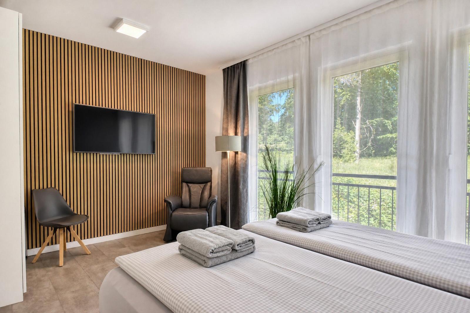 Zimmer mit Doppelbett, TV, Sessel und Blick auf Grünfläche.