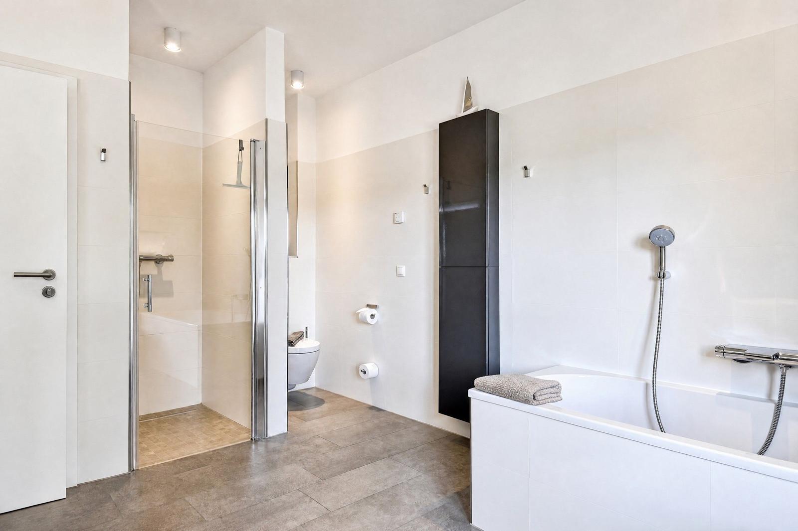 Badezimmer mit Dusche, Toilette und Badewanne. Schwarzer Schrank und graue Fliesen.