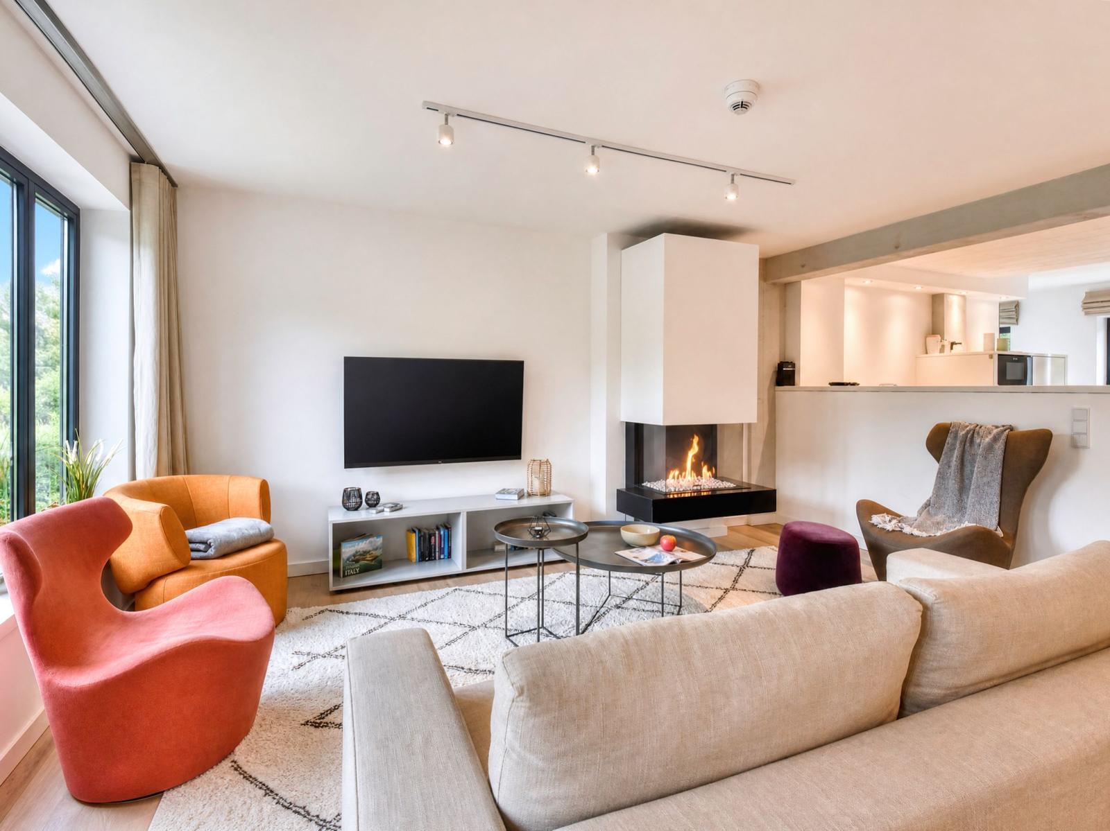 Wohnzimmer mit Sofa, Sesseln und Kamin. Fernseher und Wohnbereich sind sichtbar.