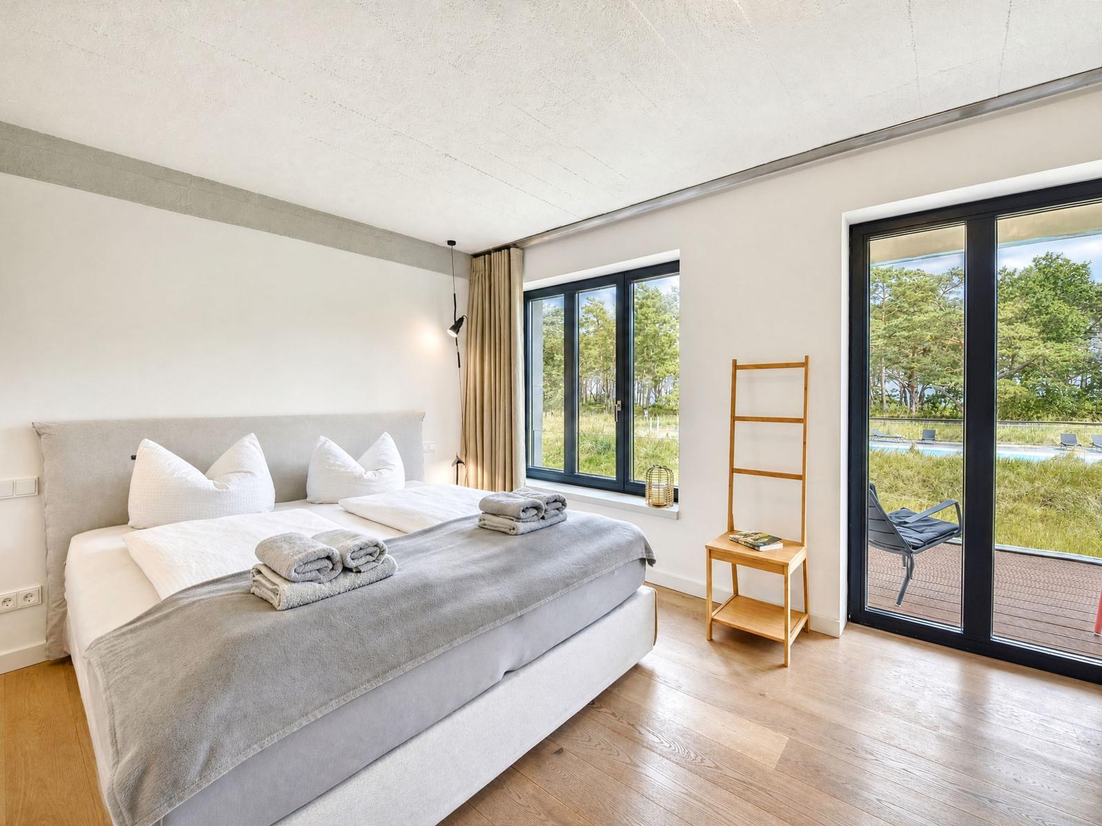 Schlafzimmer mit Doppelbett, Holzboden und Blick auf Pool und Garten.