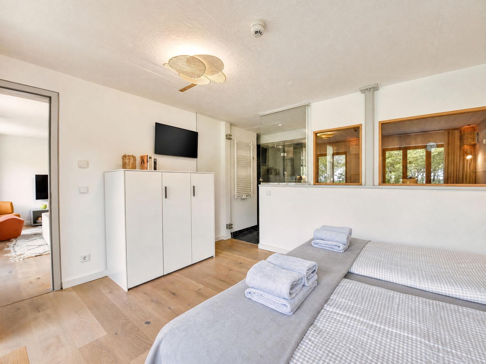 Zimmer mit Doppelbett, Kleiderschrank und TV. Durchgang zur Sauna und Wohnbereich.