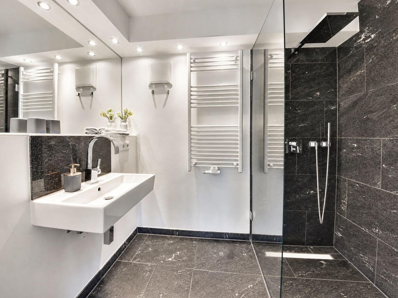 Badezimmer mit Dusche, Waschbecken und Heizkörper.