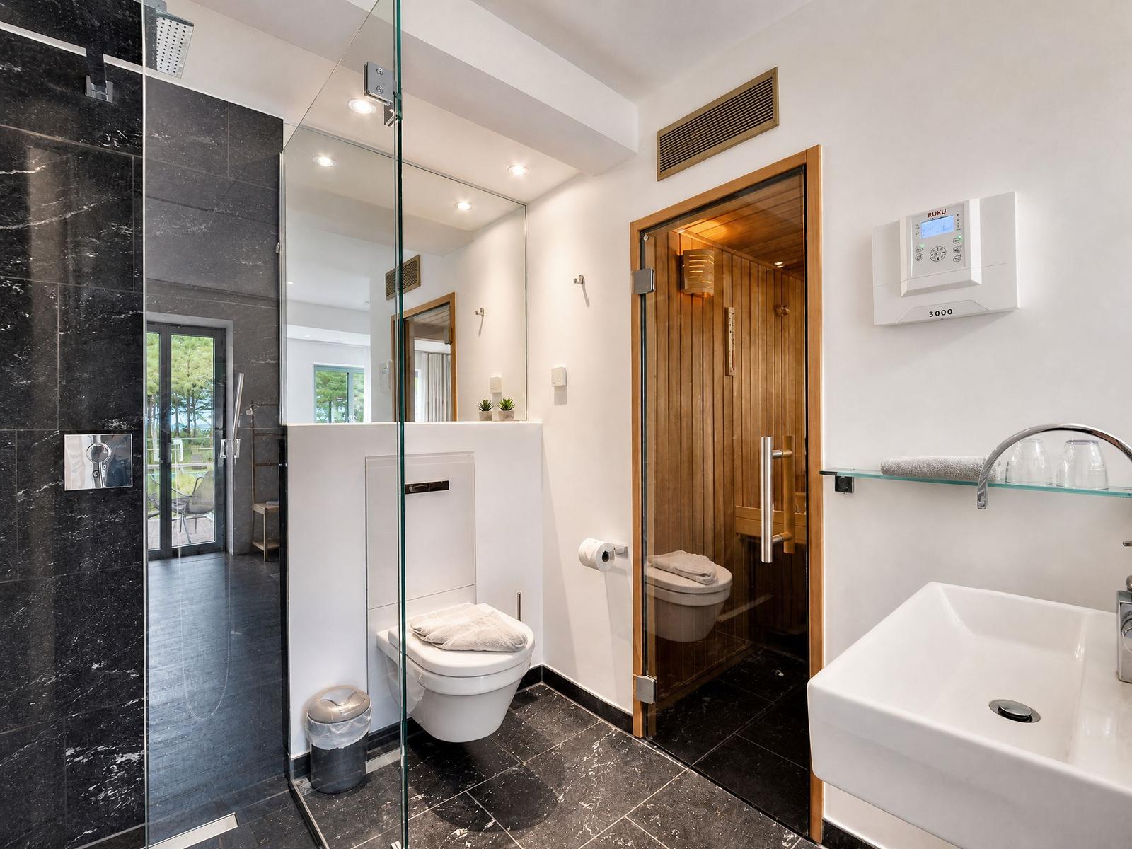 Badezimmer mit Dusche, Toilette und Sauna. Schwarze Fliesen und weiße Wand.