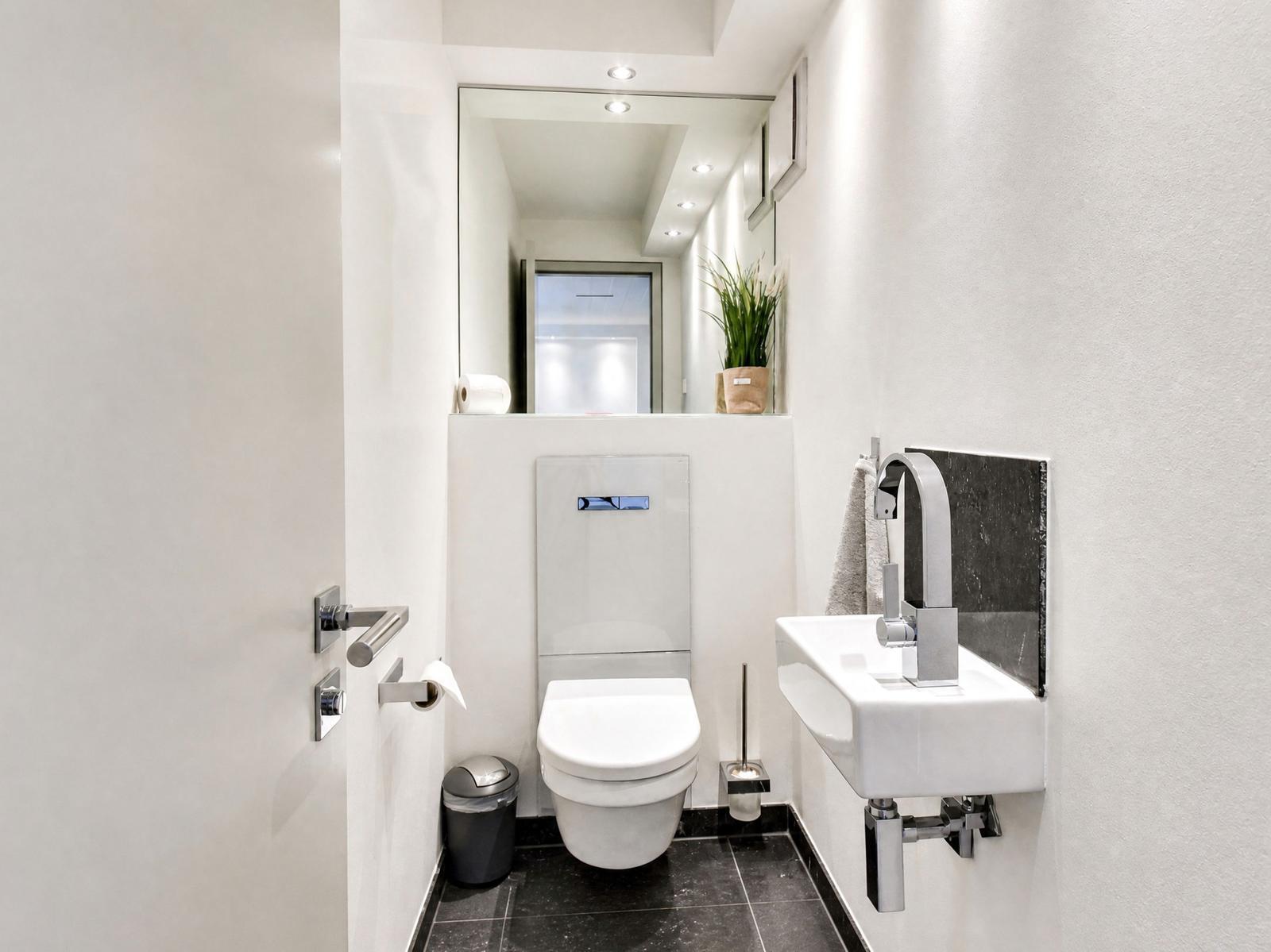 Dusche mit modernem Waschbecken und Toilette. Schwarze Fliesen und Spiegel.