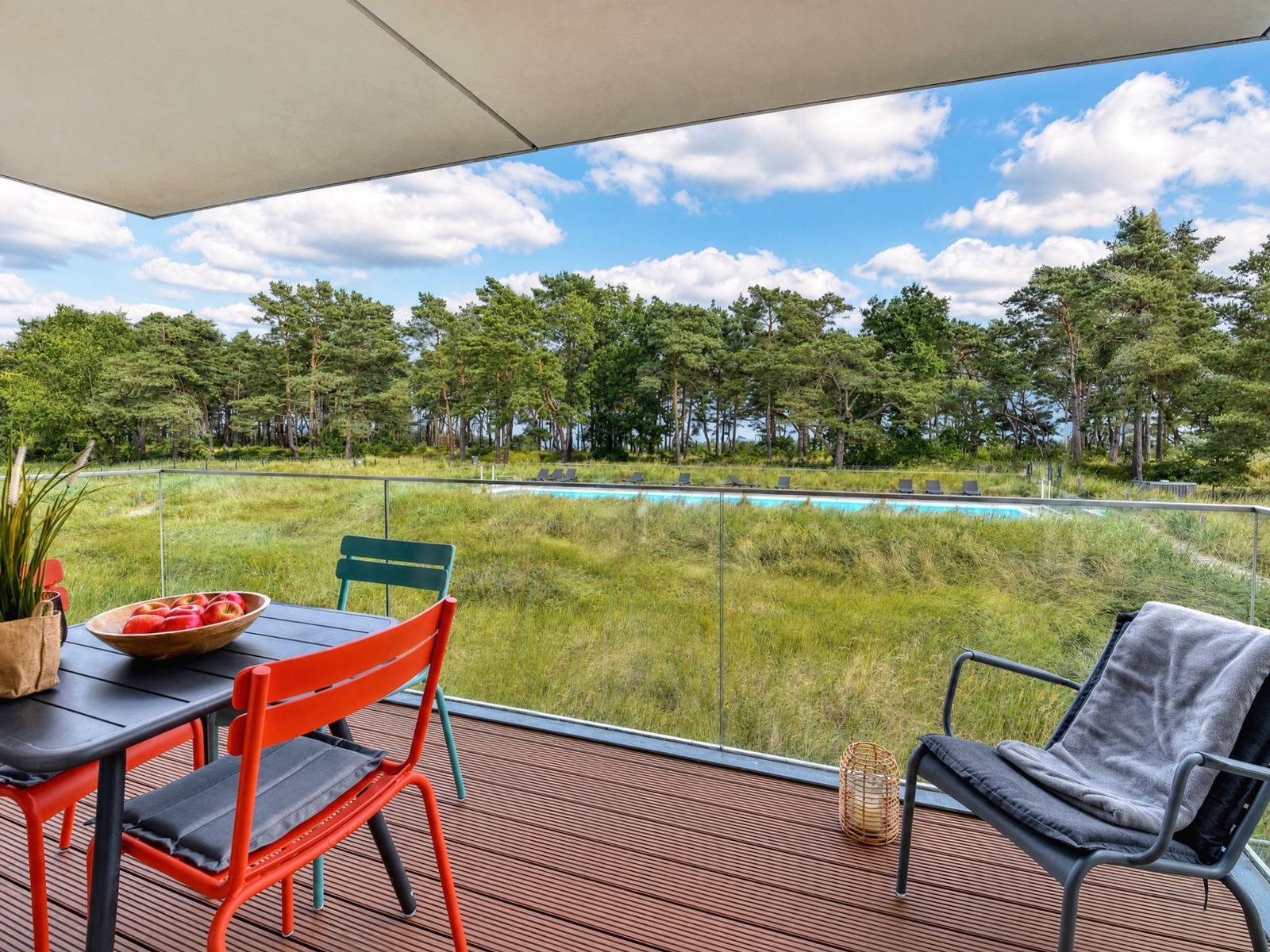 Terrasse mit Tisch, Stühlen und Blick auf Pool und Wald.