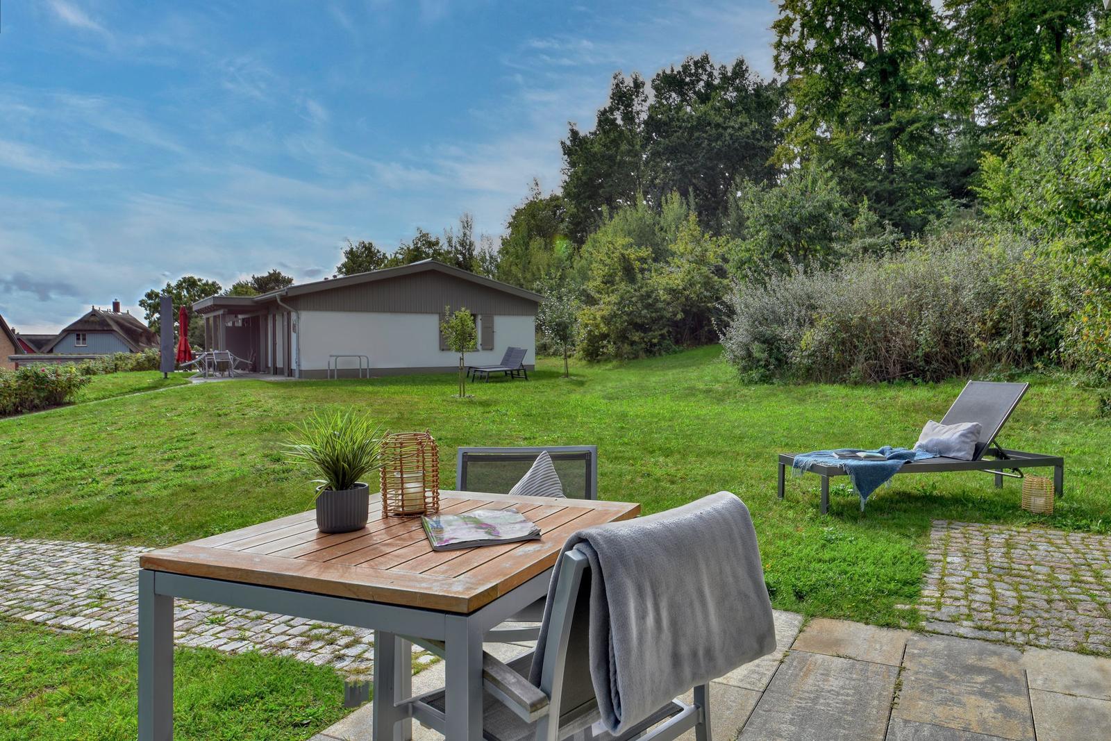Garten mit Tisch, Stühlen und Liege. Im Hintergrund das Haus und Bäume.