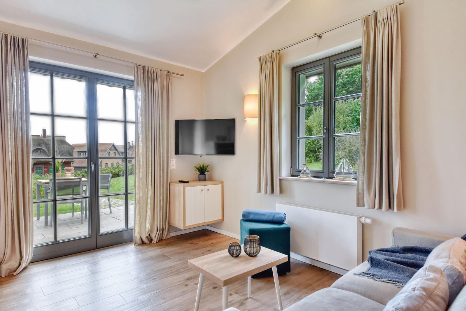 Wohnzimmer mit Sofa, Couchtisch, Fernseher und Fenster zur Terrasse.
