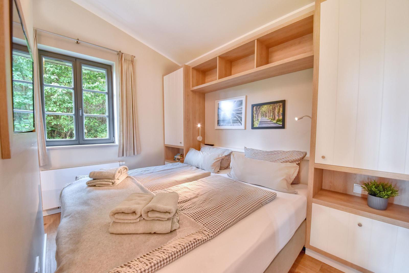 Schlafzimmer mit Doppelbett, Fenster mit Blick auf Bäume und integrierte Schränke.