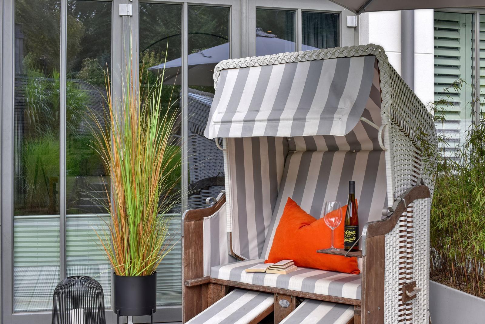 Hochwertiger Strandkorb mit orangefarbenem Kissen und Wein auf Terrasse.