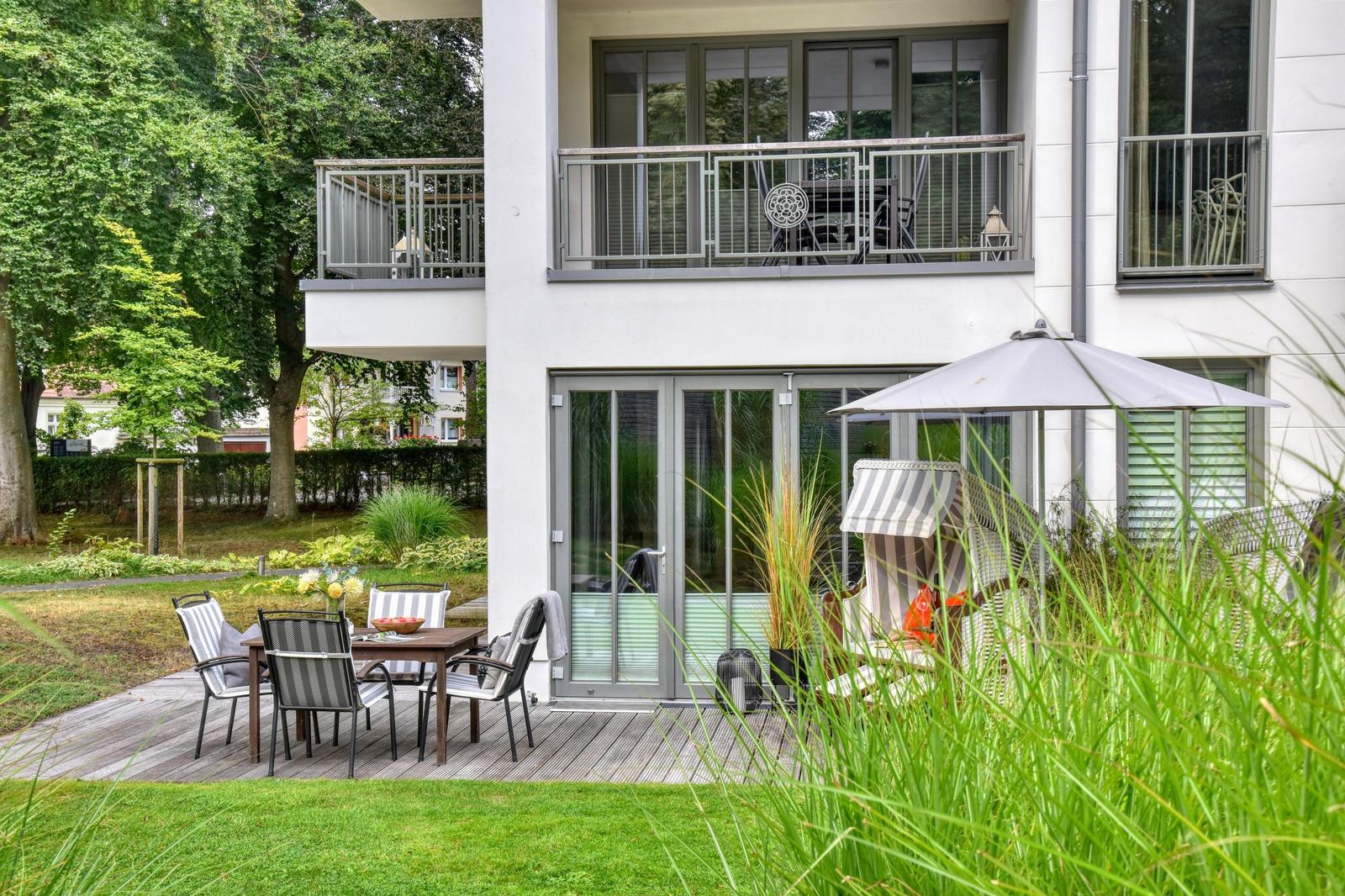 Terrasse mit Tisch, Stühlen und Sonnenschirm. Hinterhof mit Grünflächen und Balkon.