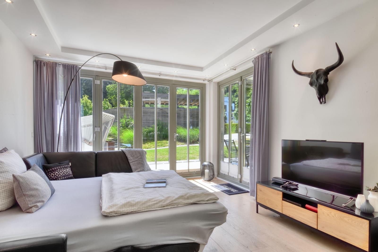 Ein Wohnzimmer mit Sofa, Fernseher und Blick auf den Garten.