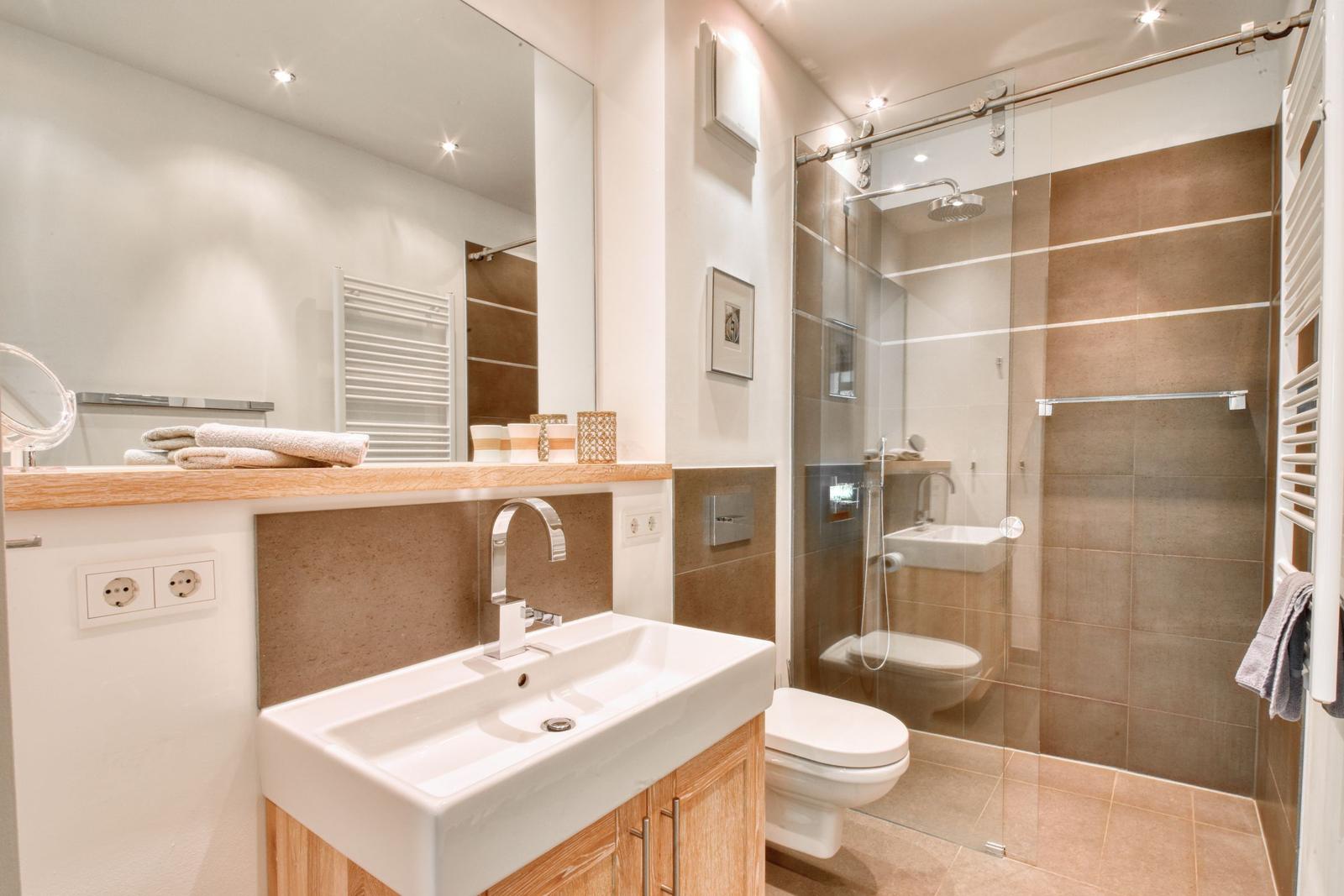 Badezimmer mit Dusche, Waschbecken und Toilette. Holzunterschrank und Spiegel.