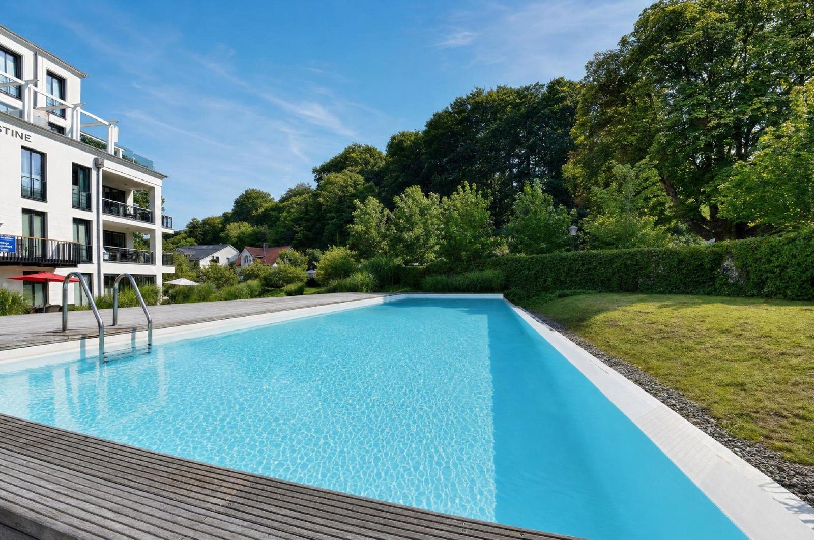 Pool mit Holzdecke, umgeben von Grün und einem Gebäude.