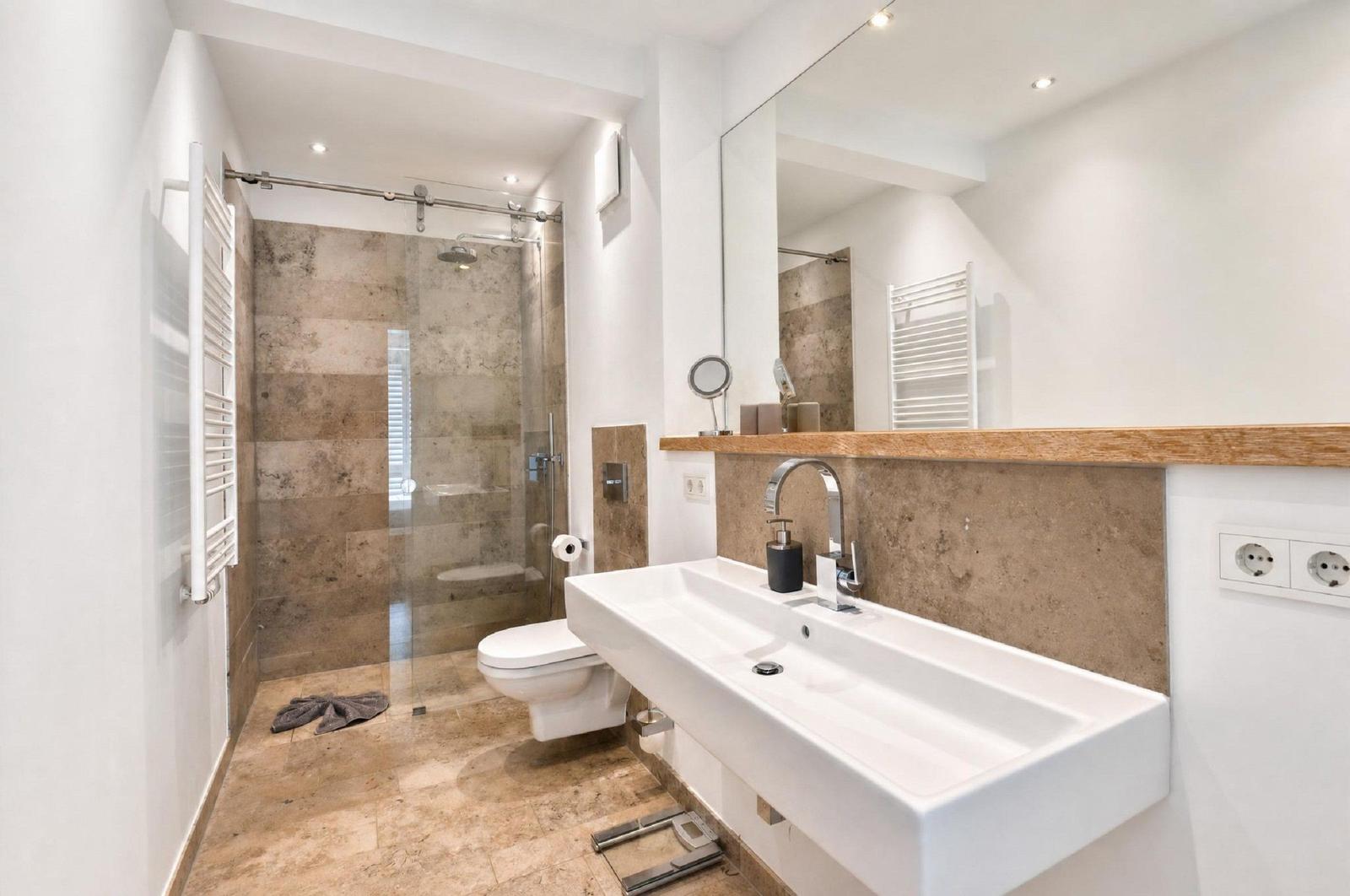 Bad mit Dusche, Waschbecken und Toilette. Holz-Arbeitsplatte und Spiegel.