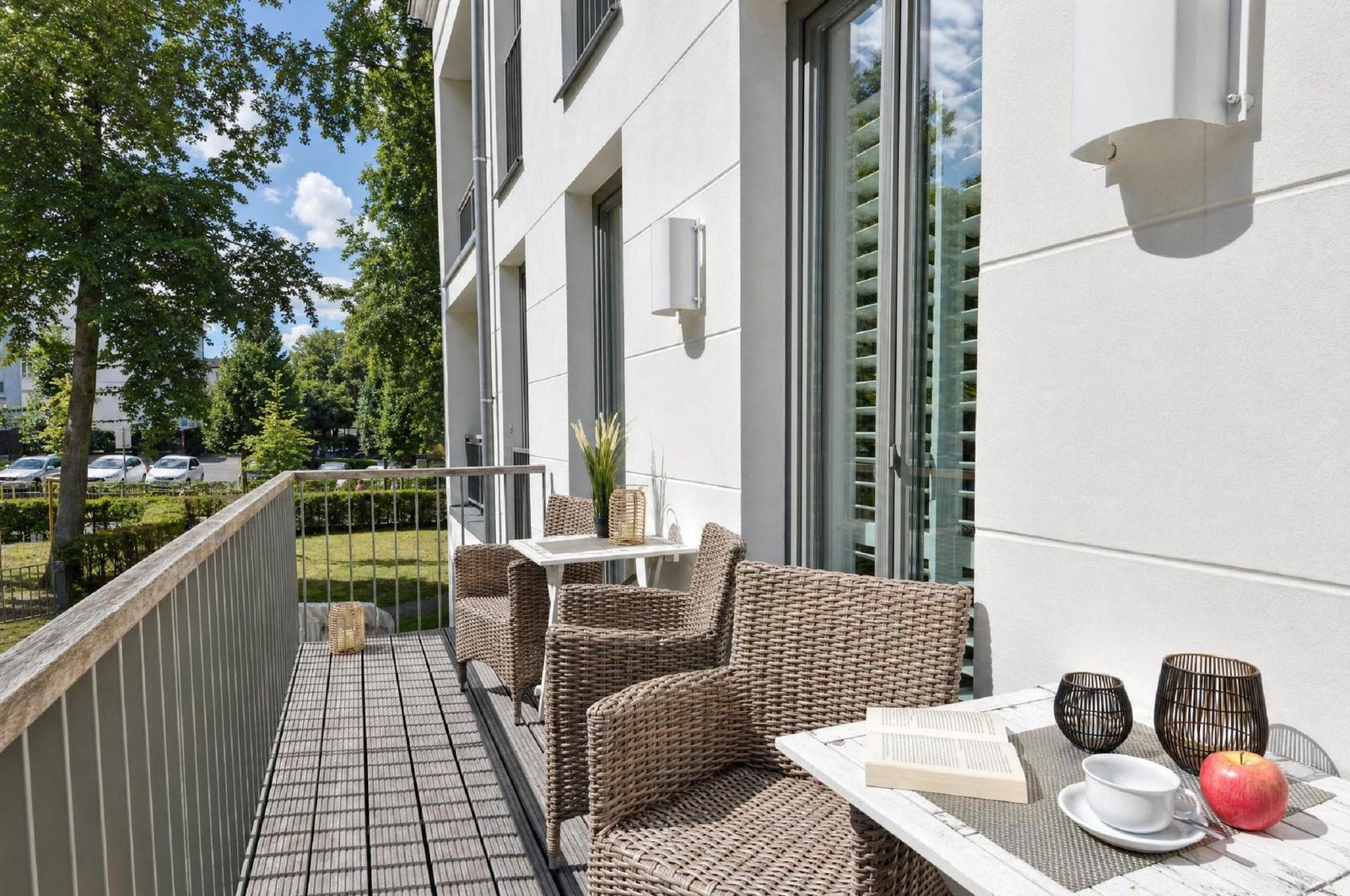Terrasse mit Wickerstühlen, Tisch und Blick auf Grünfläche.