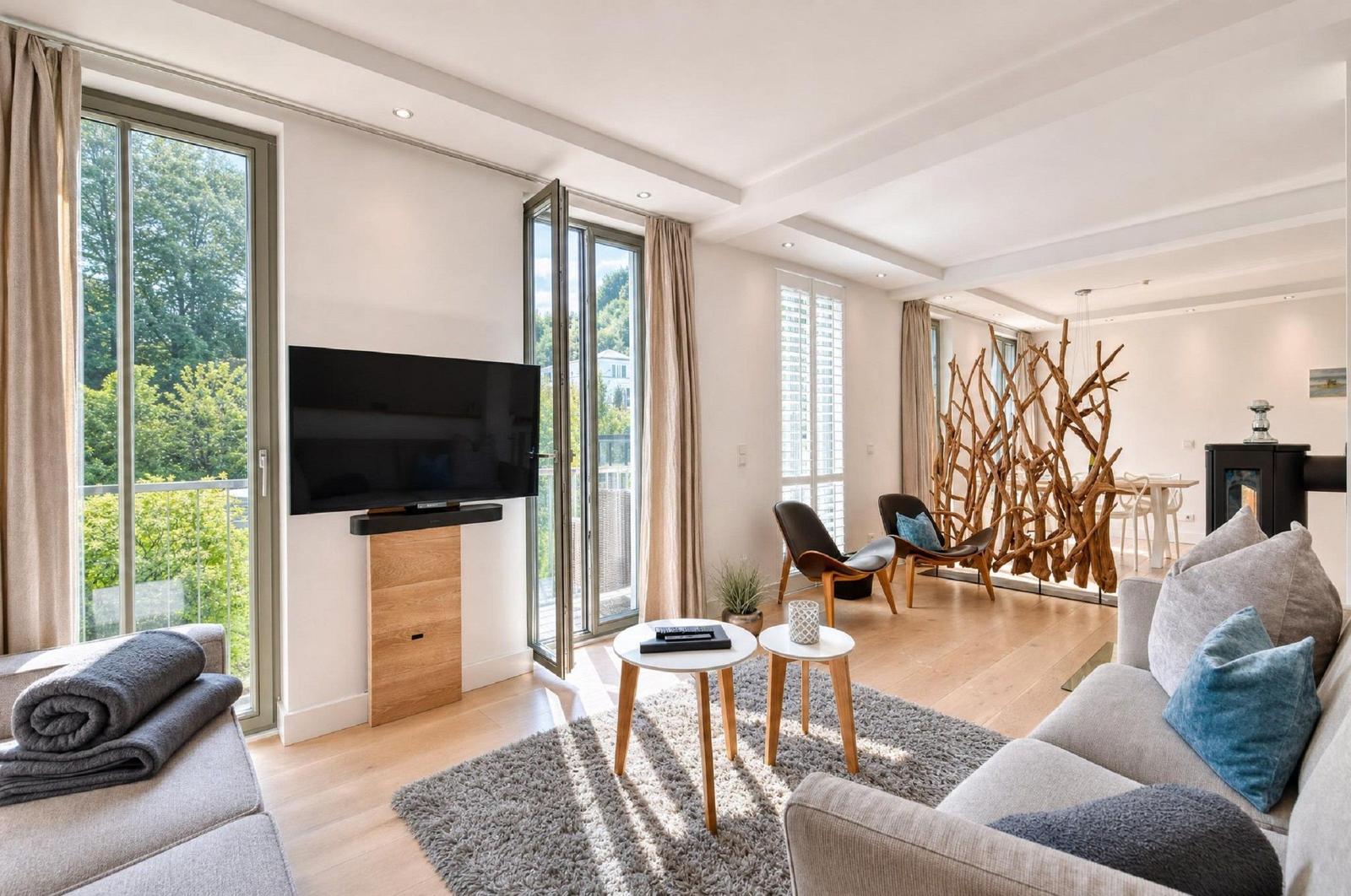 Wohnzimmer mit TV, Sofa, Tischen und Blick auf Balkon. Hölzerne Dekoration trennt Raum.