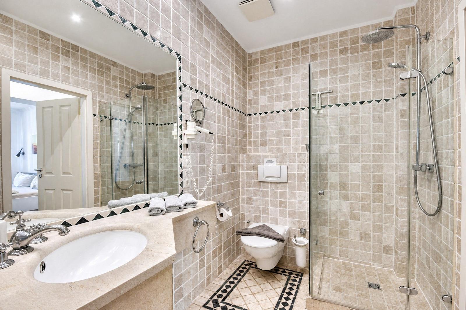Badezimmer mit Dusche, Waschbecken und Toilette. Fliesenwand mit Mosaikstreifen.