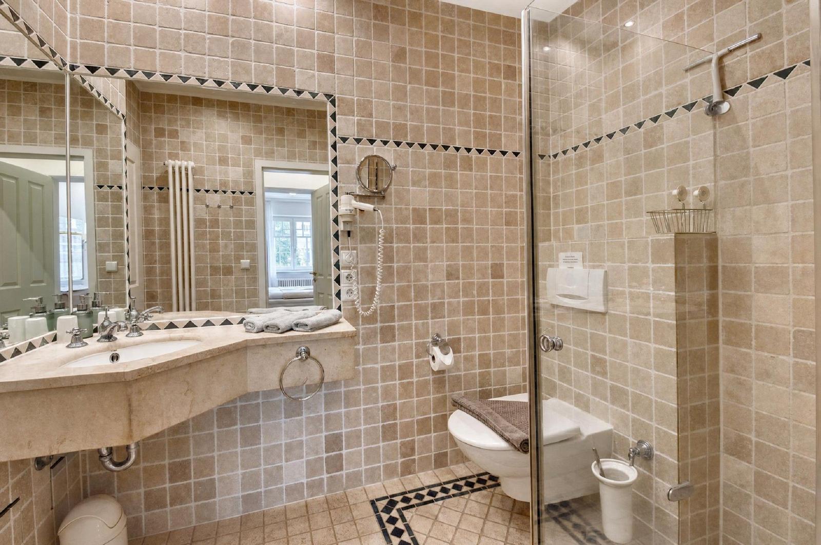 Badezimmer mit Dusche, Waschbecken und Toilette. Fliesen mit dekorativen Akzenten.