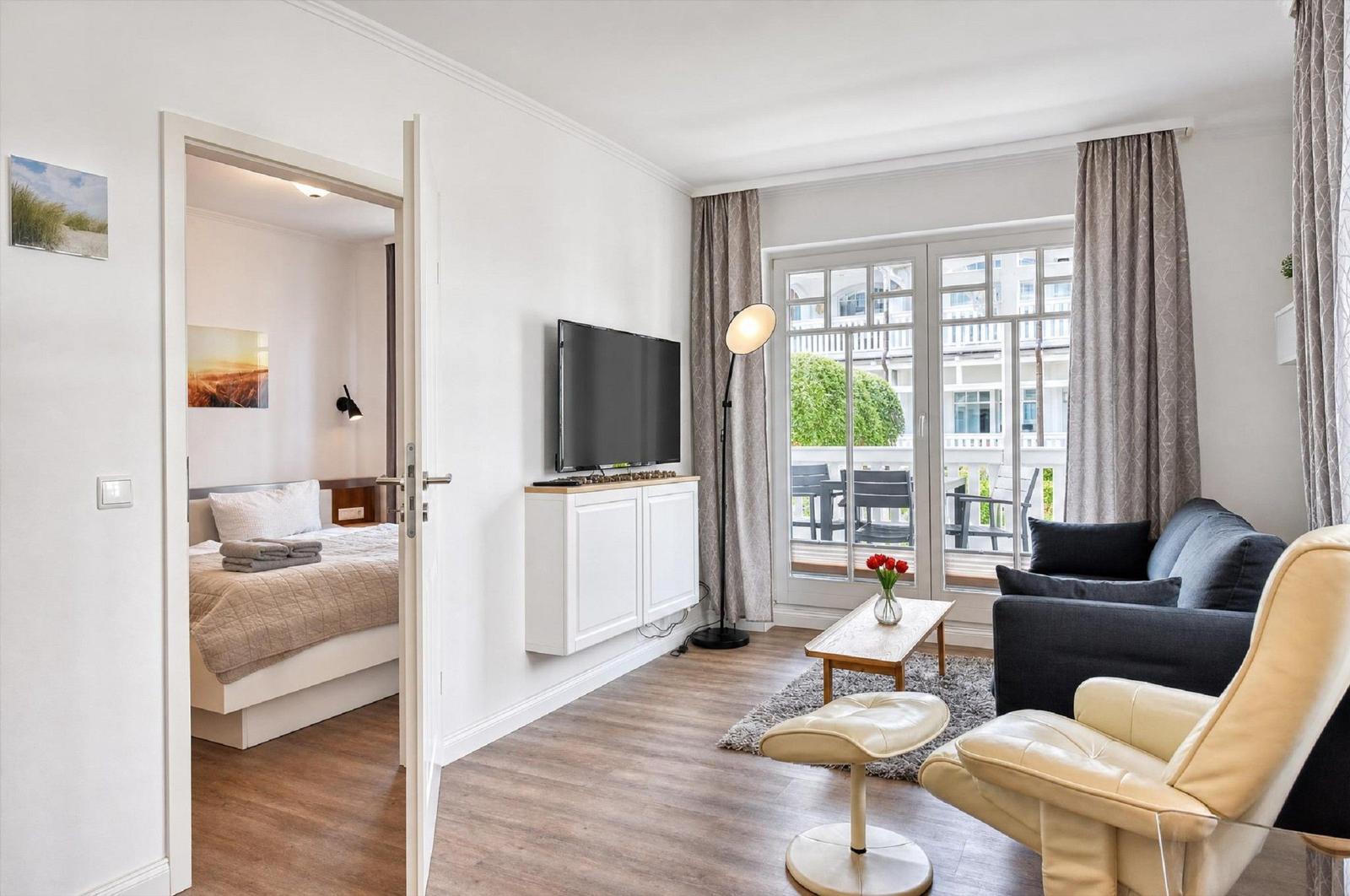 Wohnzimmer mit Sofa, Fernseher und Balkon. Durchgang zur Schlafzimmer.