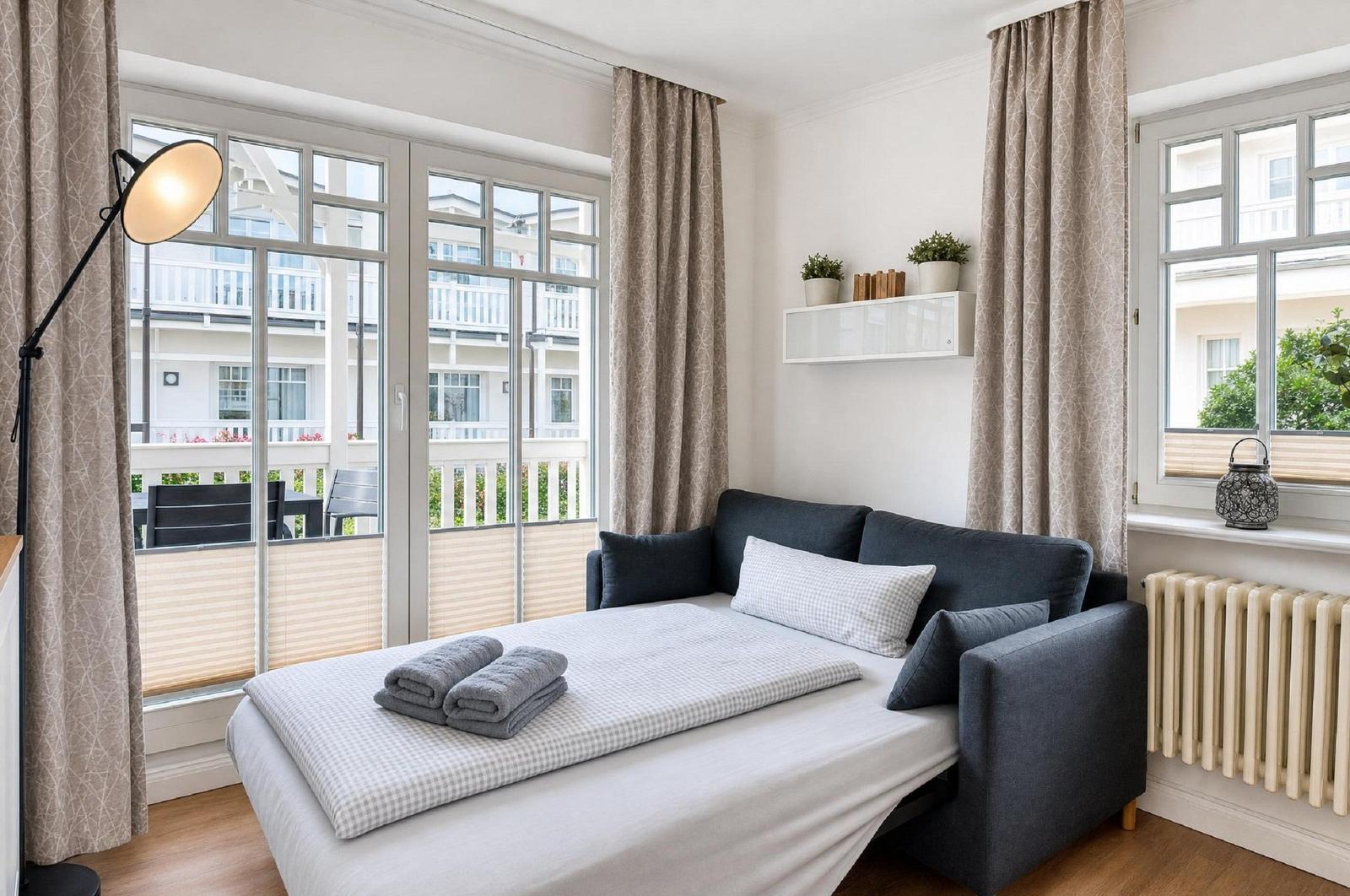 Schlafzimmer mit Sofa-Bett, großen Fenstern und Balkonansicht.