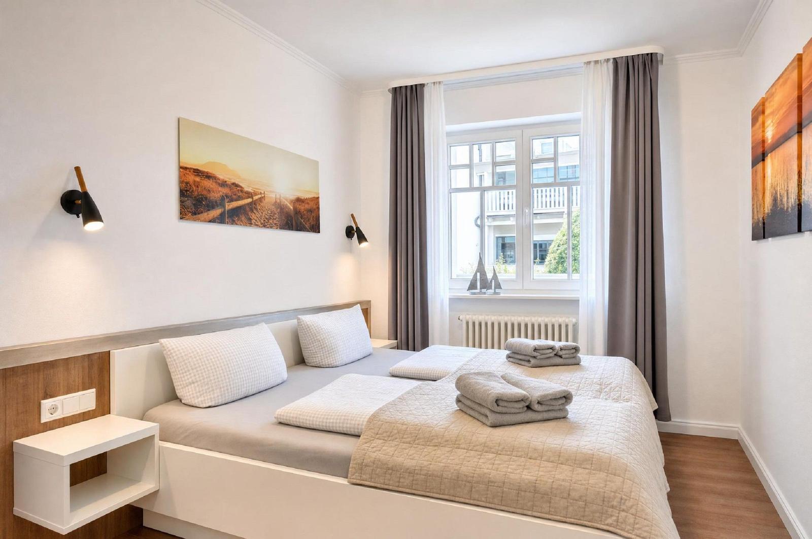 Schlafzimmer mit Doppelbett, Fenster und Wandbildern.