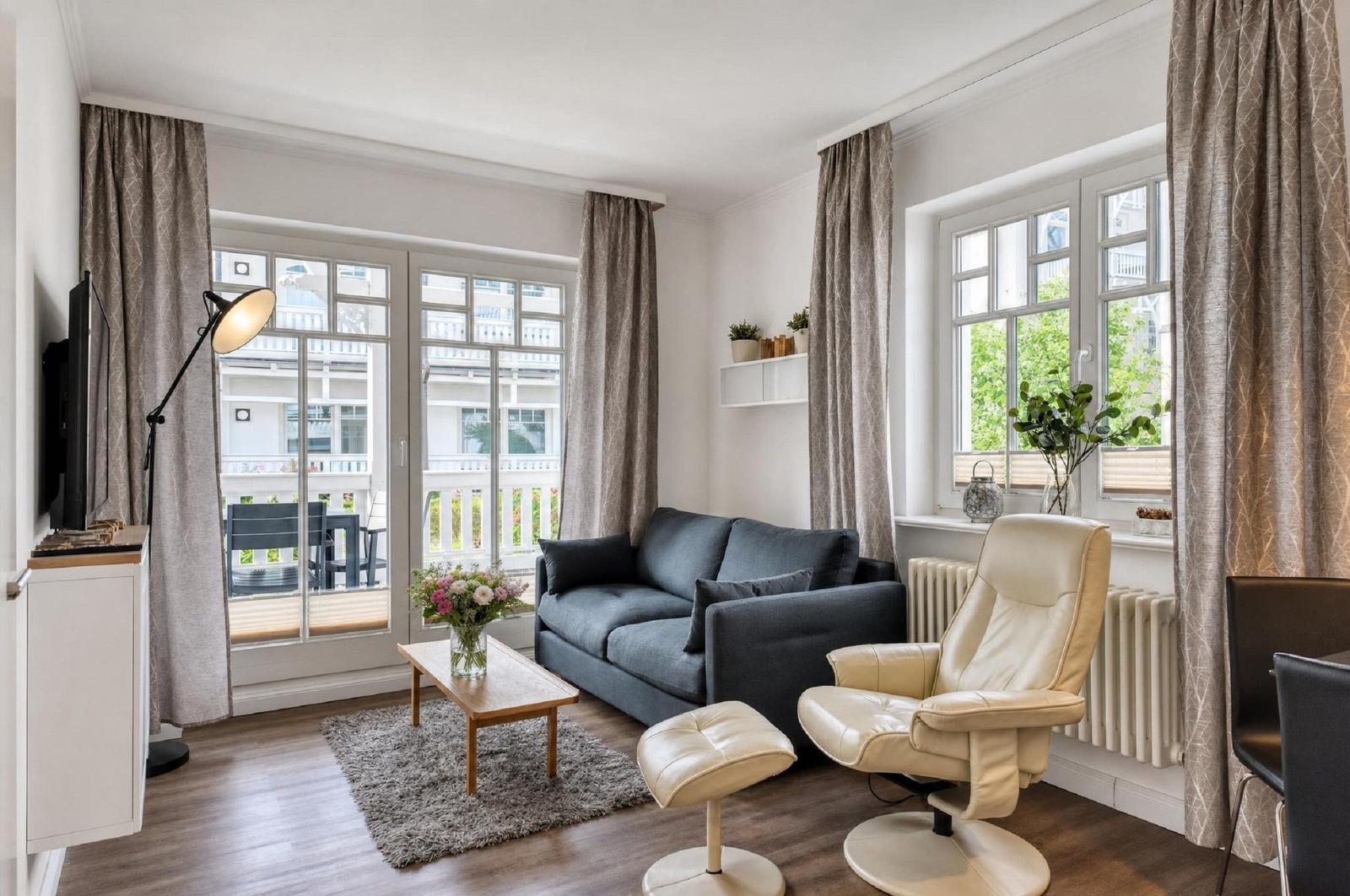 Wohnzimmer mit Sofa, Sessel, Couchtisch und Fenstern.