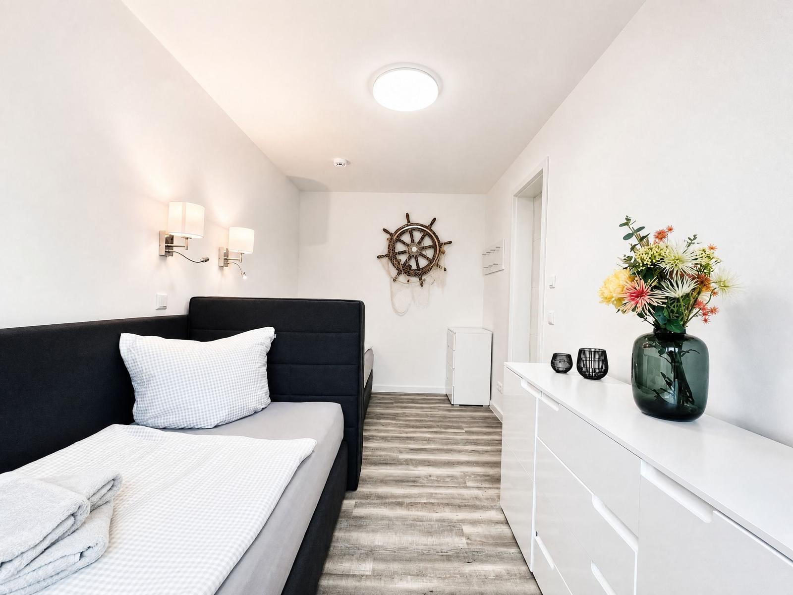 Bedroom with bed, dresser, and ships wheel on the wall.