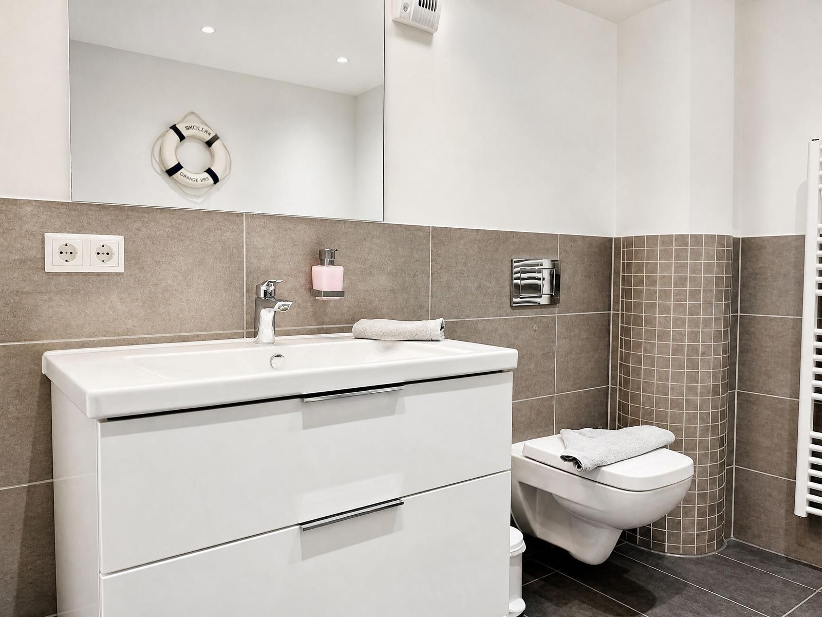 Bathroom with sink, mirror, and toilet. Walls covered with gray tiles.