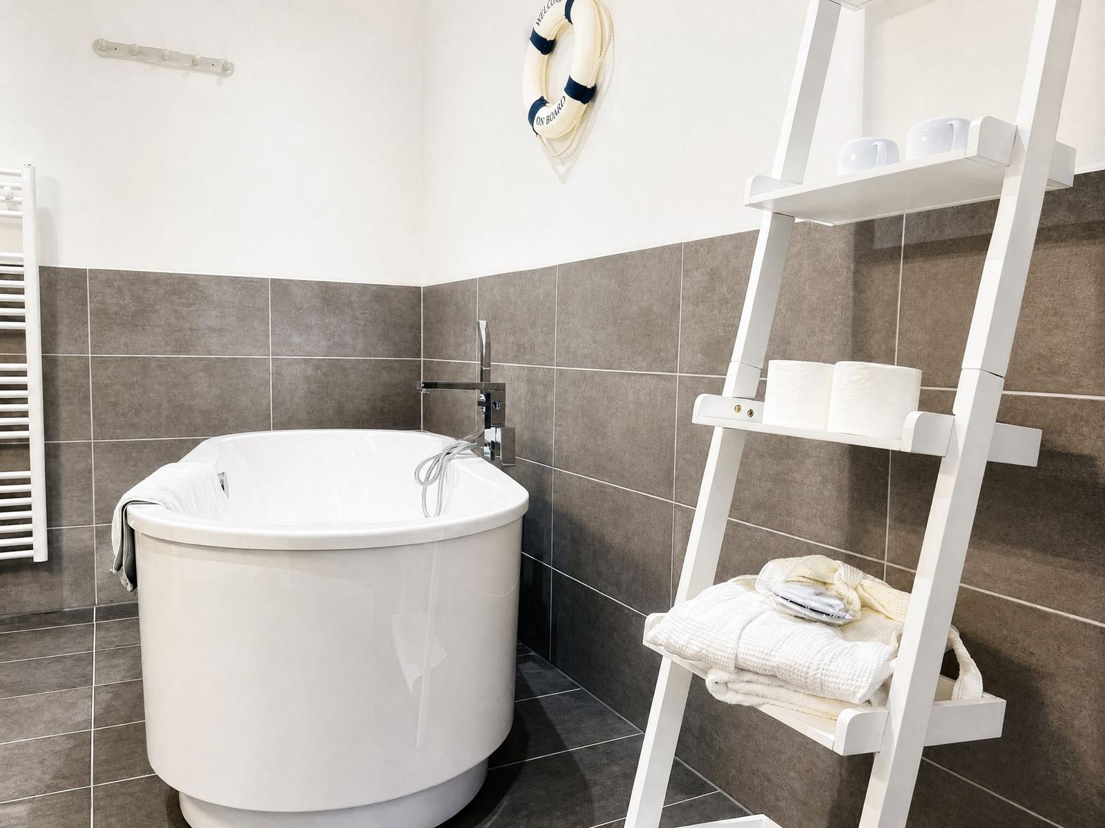 Bath with freestanding bathtub, shower head, towel rack, and white ladder shelf.
