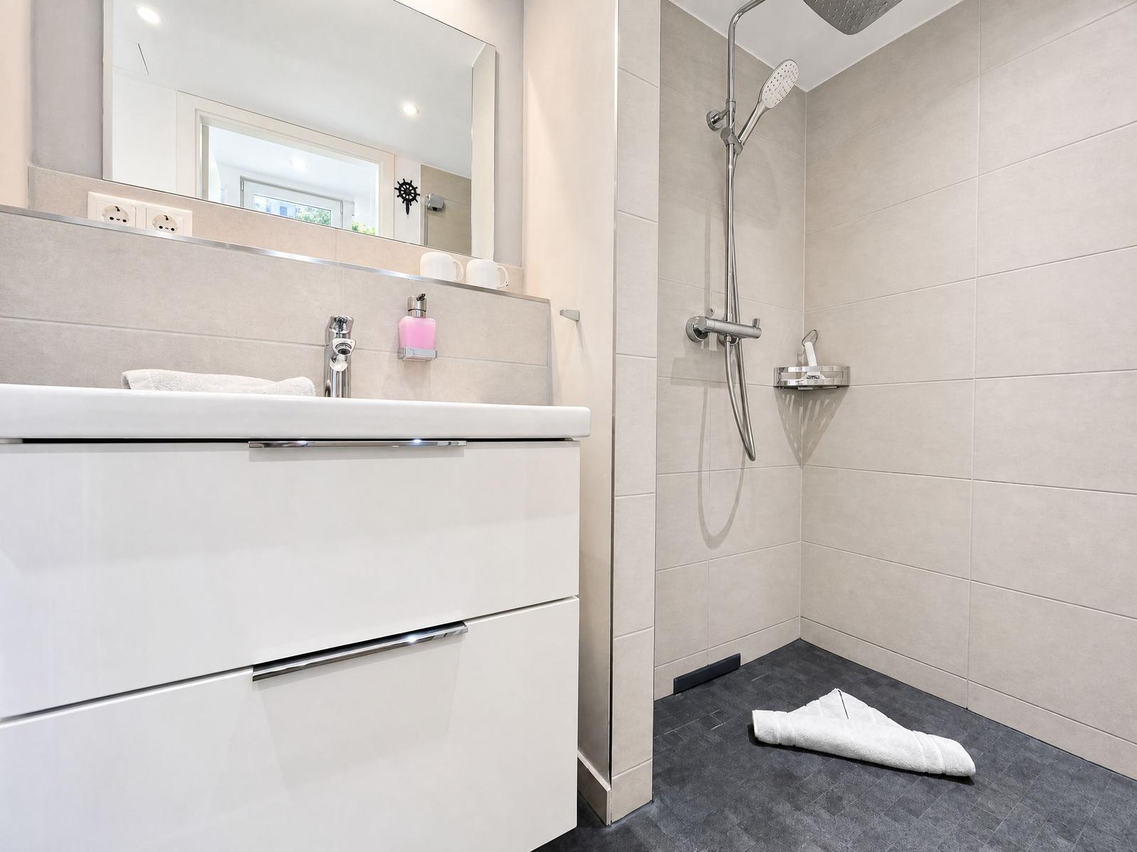 Bathroom with shower, sink, and mirror. Tile wall and white cabinet.