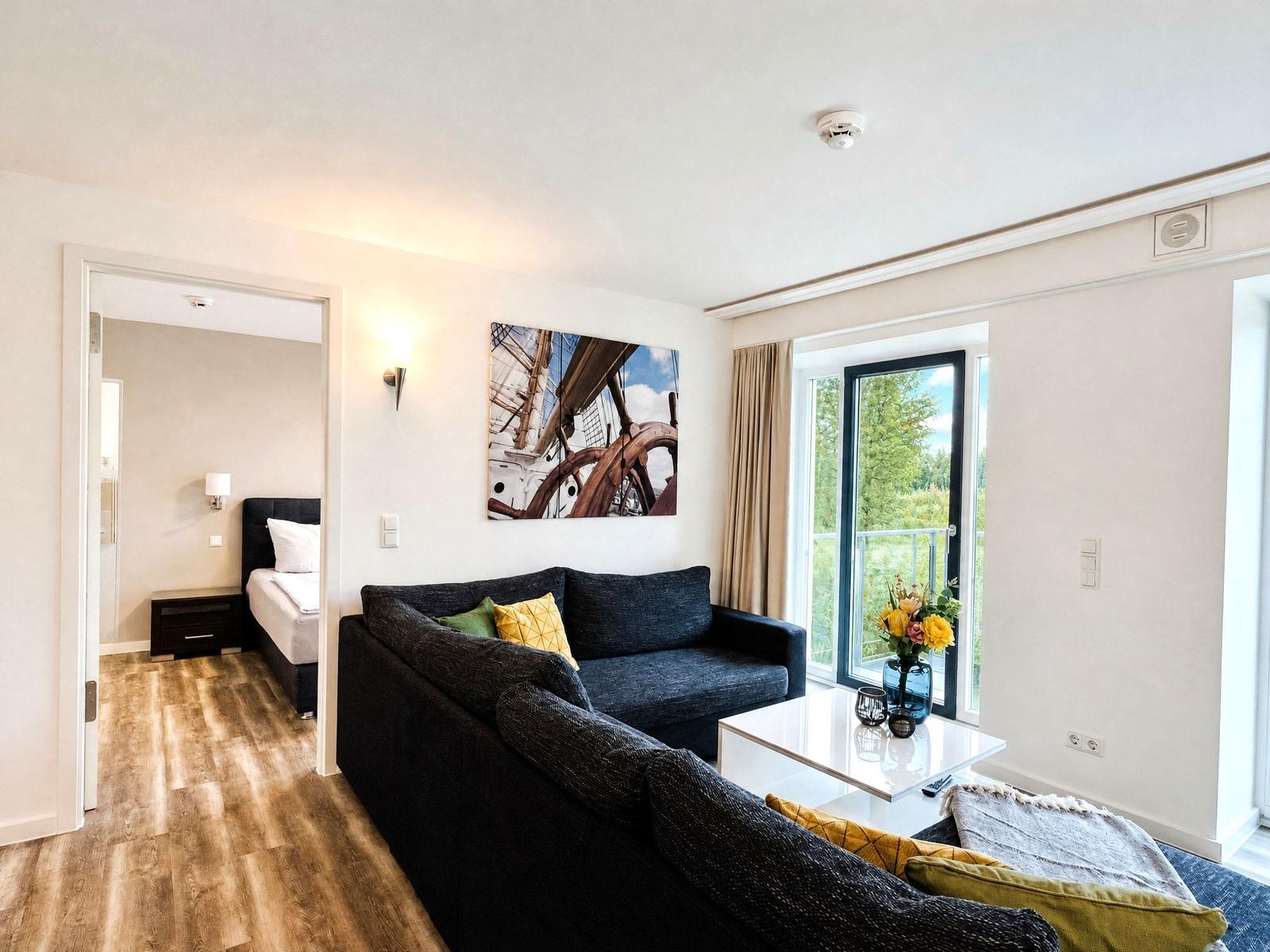 Living area with sofa, coffee table, and view to balcony. Bedroom is adjacent.