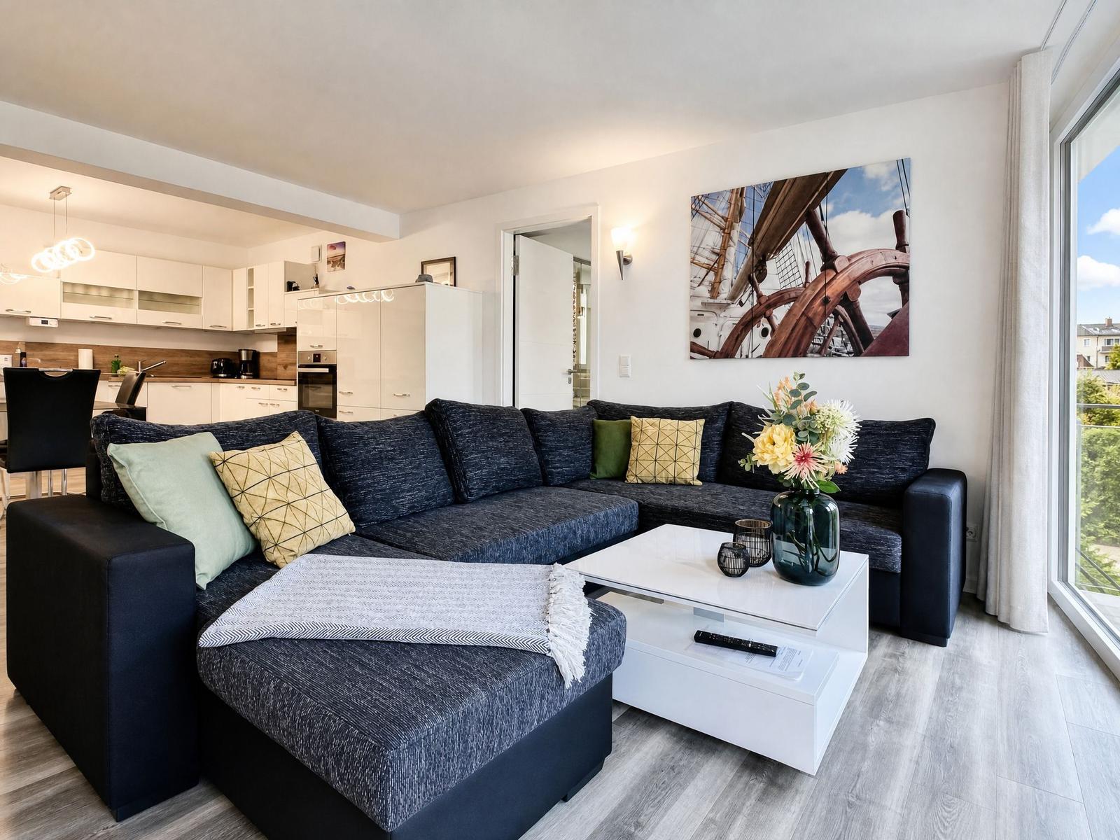 A living room with a large sofa, white coffee table, and kitchen area in the background.
