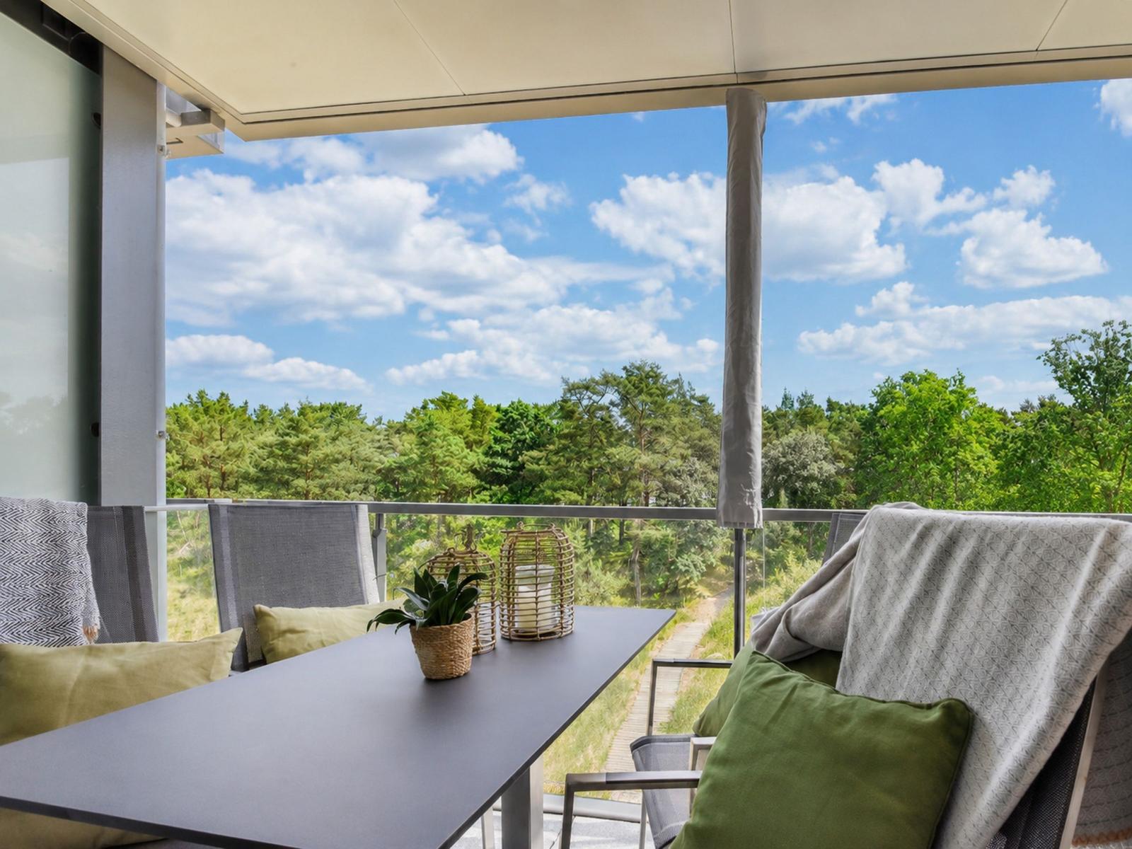Terrasse mit Tisch, Stühlen und Blick auf Wald und Himmel.