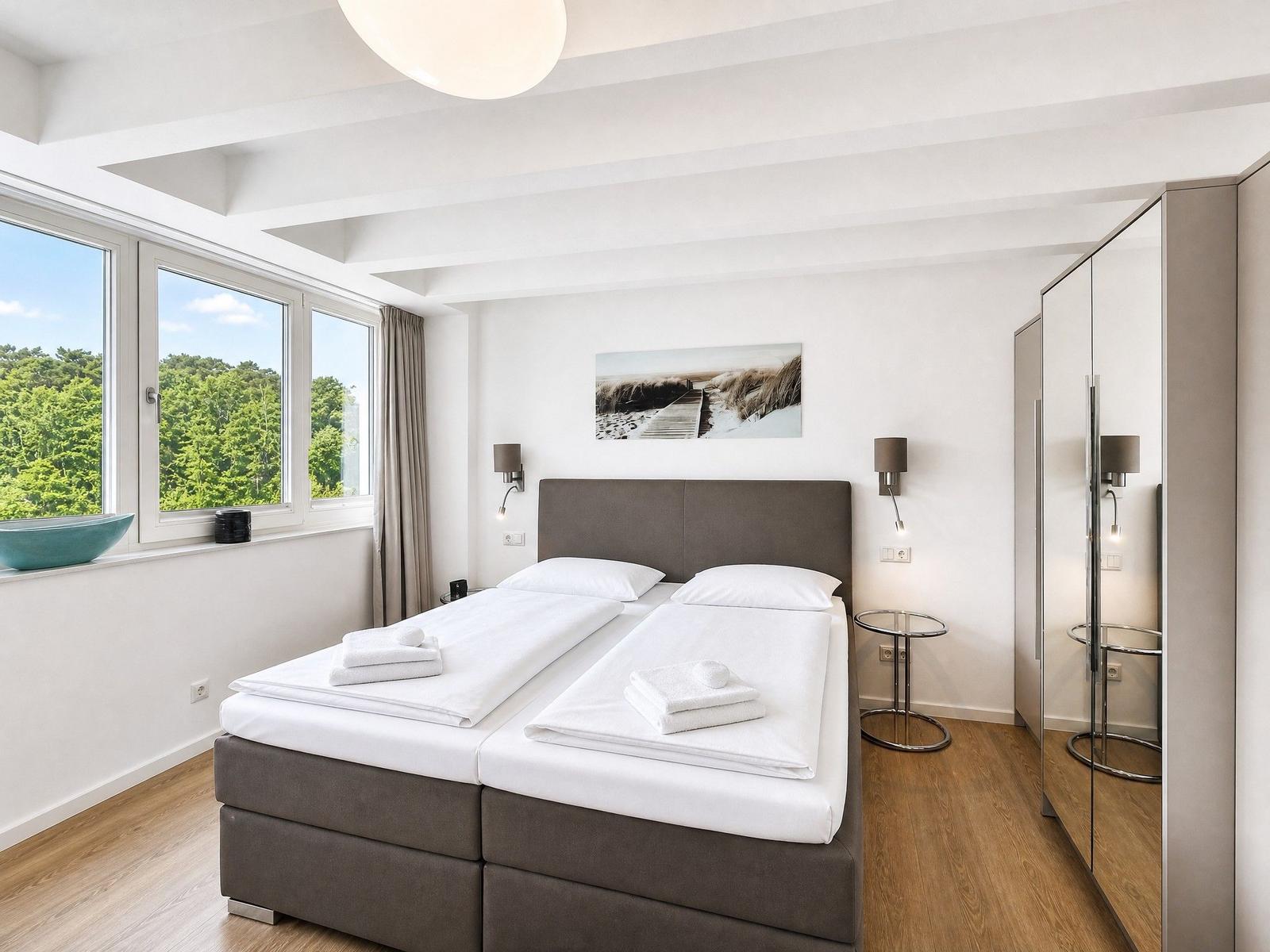 Schlafzimmer mit Doppelbett, Fenster mit Blick auf Wald und Spiegelschrank.