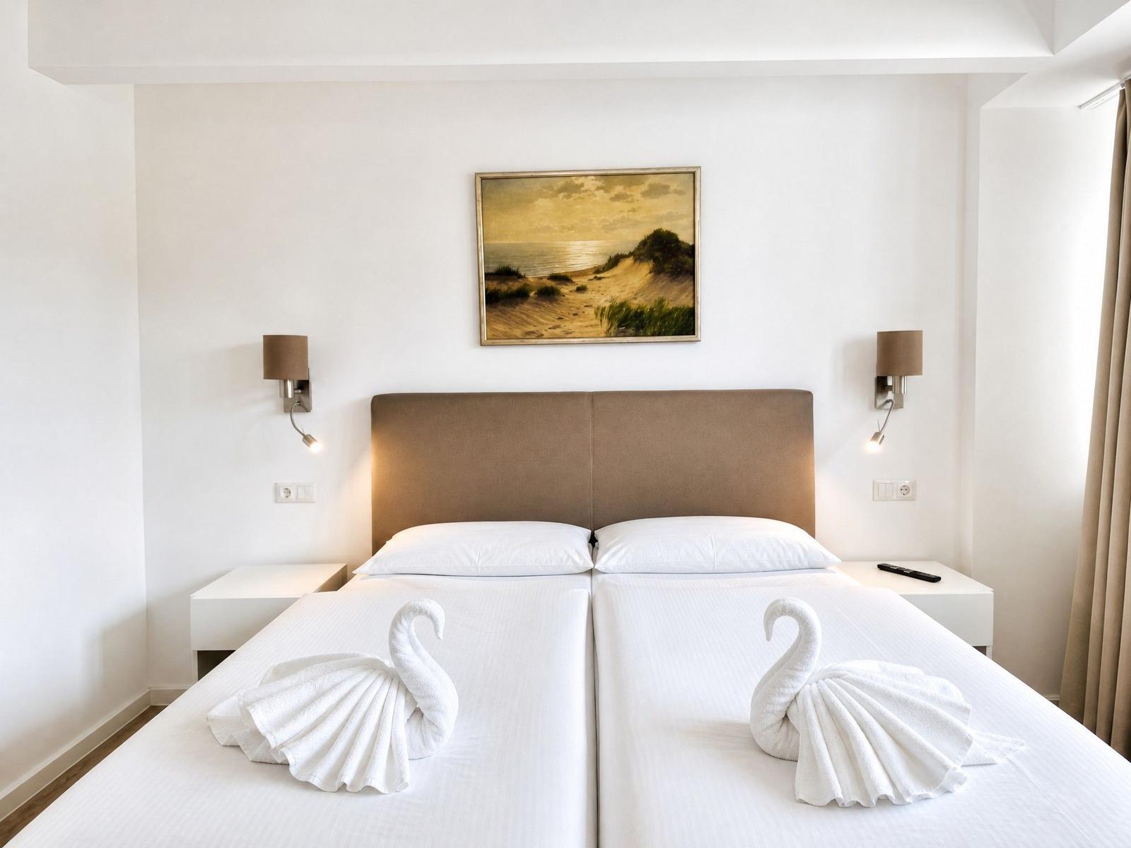 Zimmer mit Doppelbett, zwei Schwänen aus Handtüchern und Wandbild an der Wand.