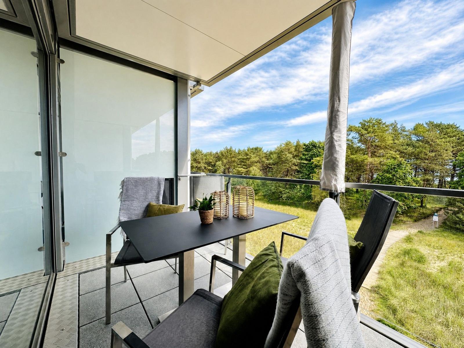 Terrasse mit Tisch, Stühlen und Blick auf Wald. Überdacht mit Sonnenschutz.