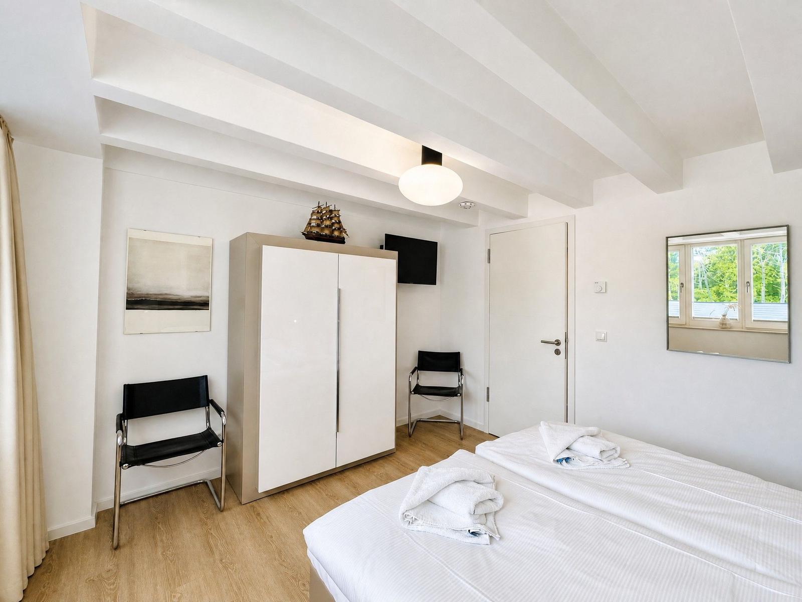 Schlafzimmer mit Bett, Kleiderschrank, Stuhl und Fenster. Decke mit Balken.