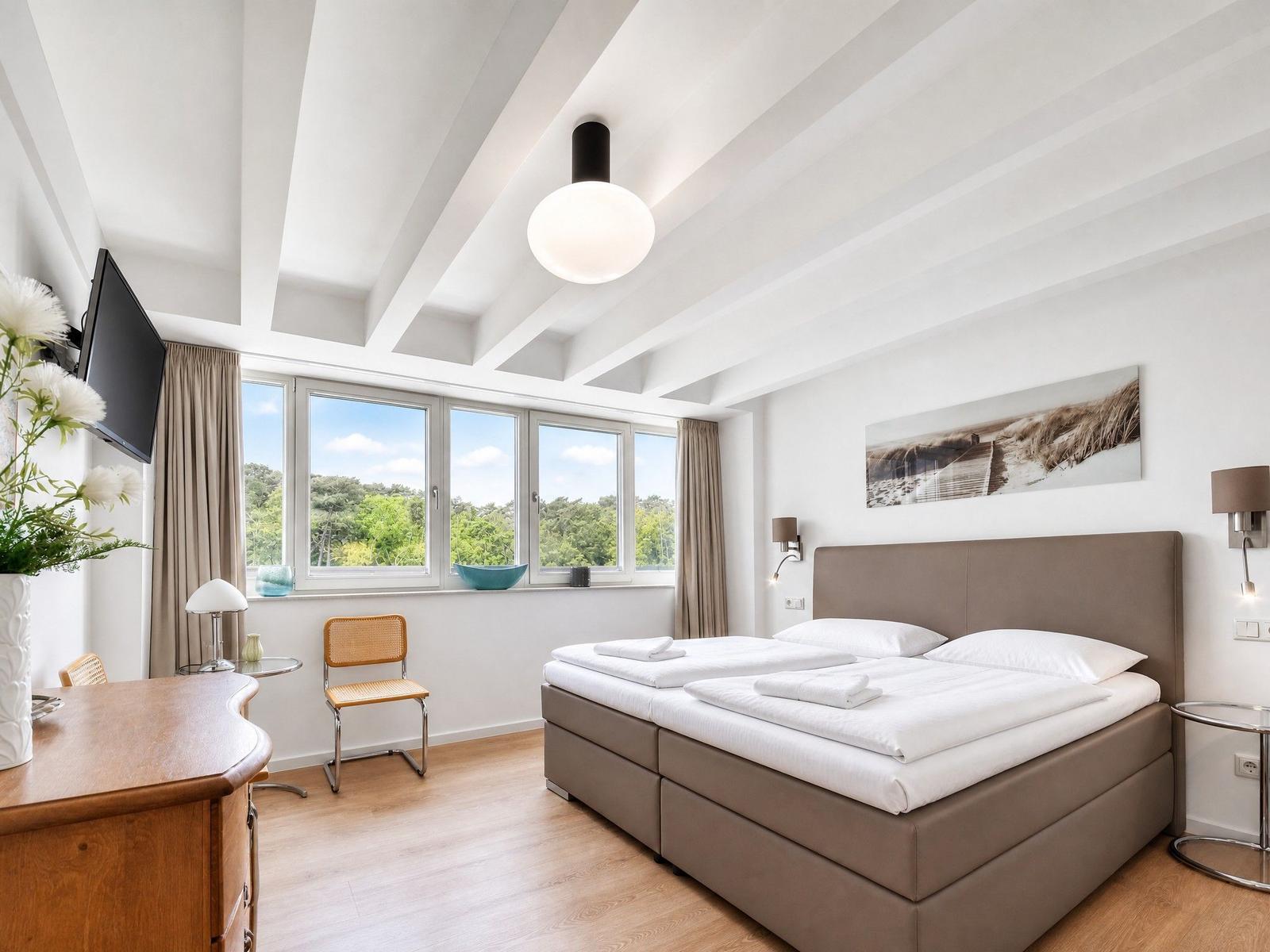 Schlafzimmer mit Doppelbett, Fenster und Schreibtisch.
